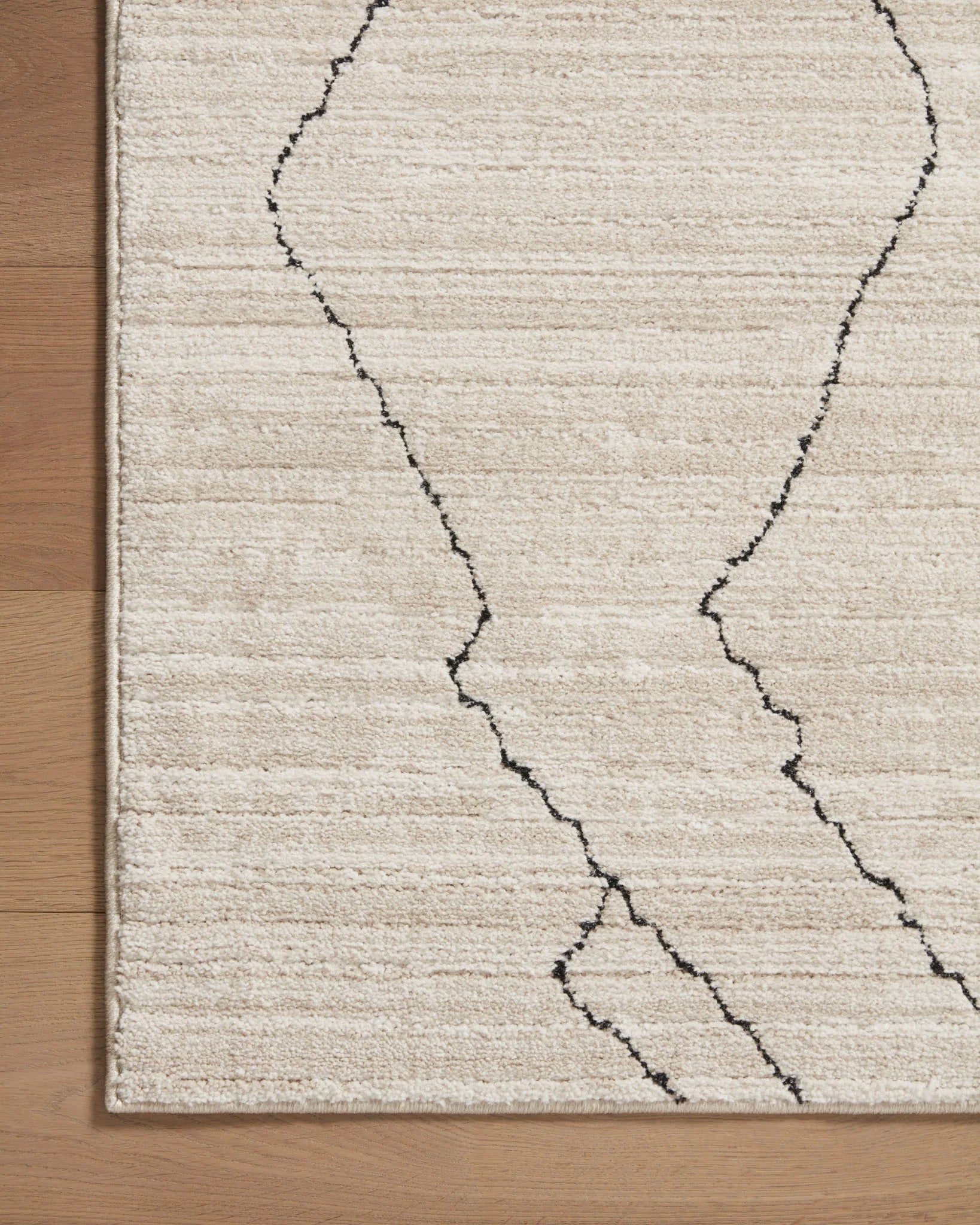 Sand area rug corner with charcoal trellis-like line pattern and low pile