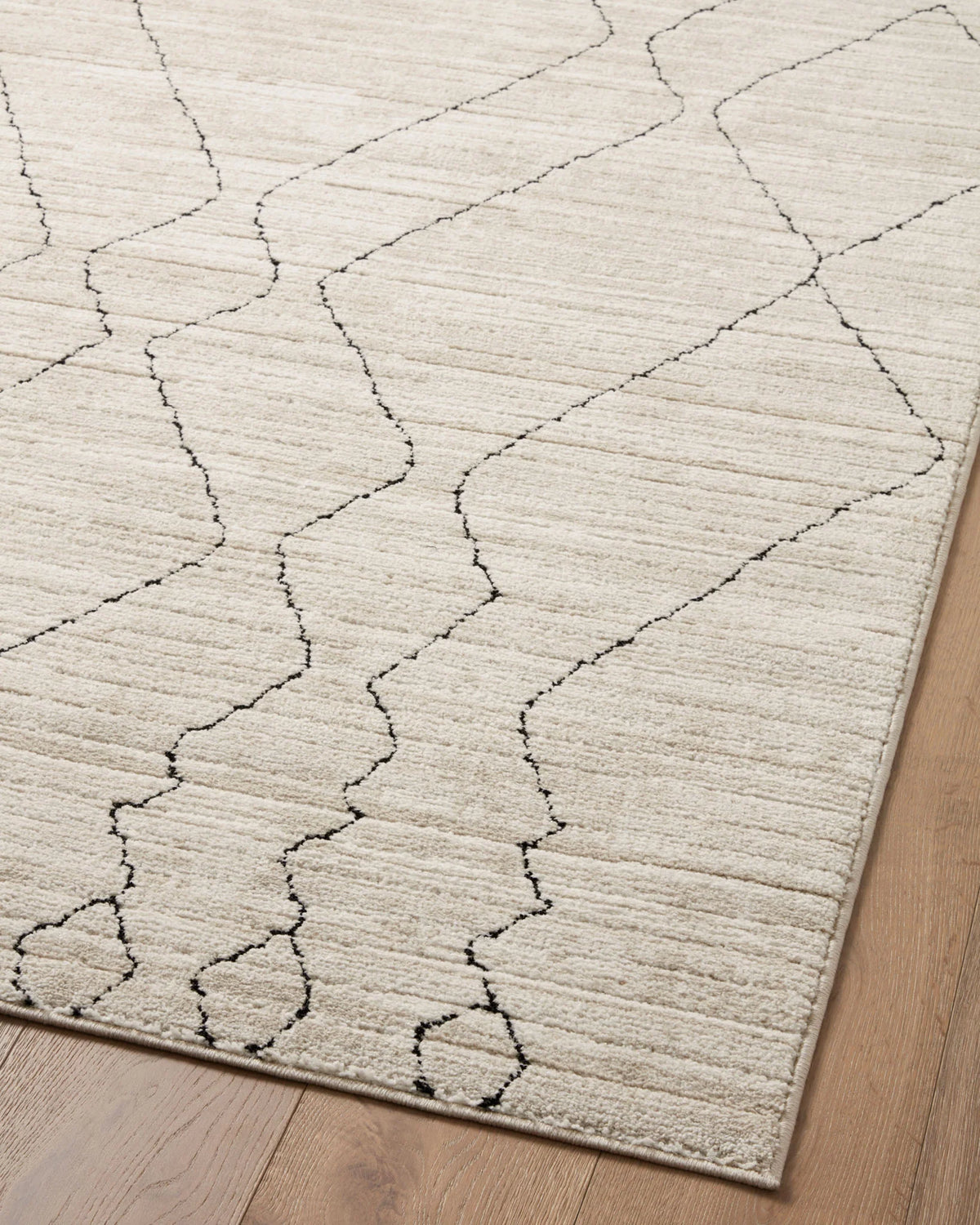 Sand area rug with charcoal linework diamond trellis pattern, corner detail.