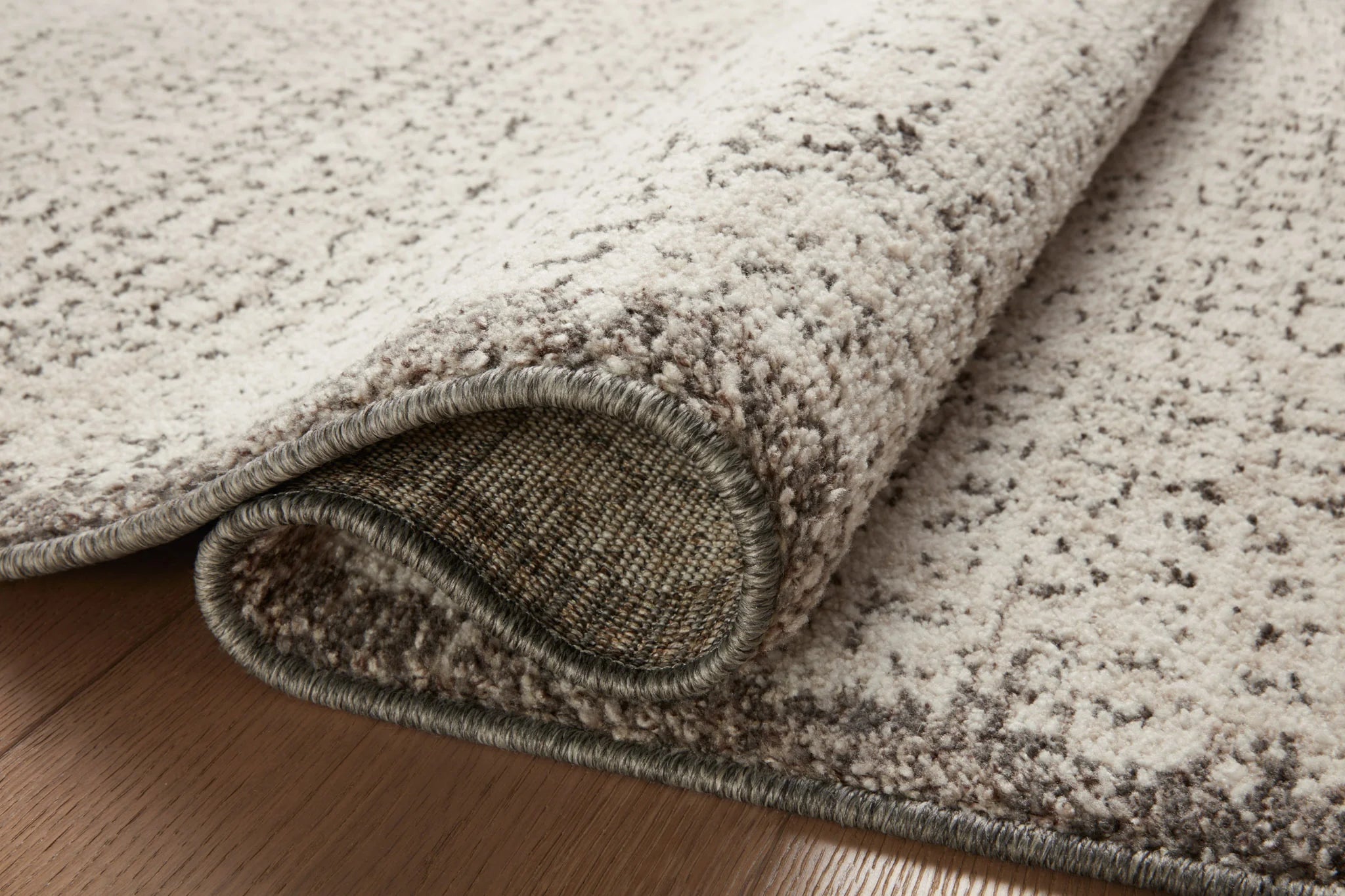 Close-up of ivory and stone accent rug rolled edge with textured weave and dark trim