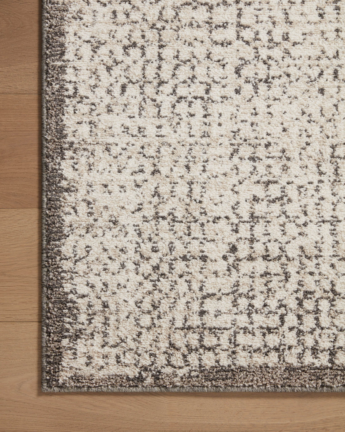 Corner view of ivory and stone accent rug with speckled pattern and border trim