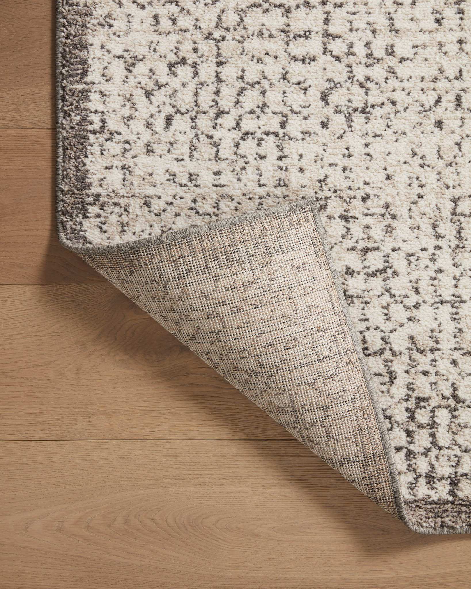 Ivory and stone area rug with speckled pattern, corner lifted to show backing