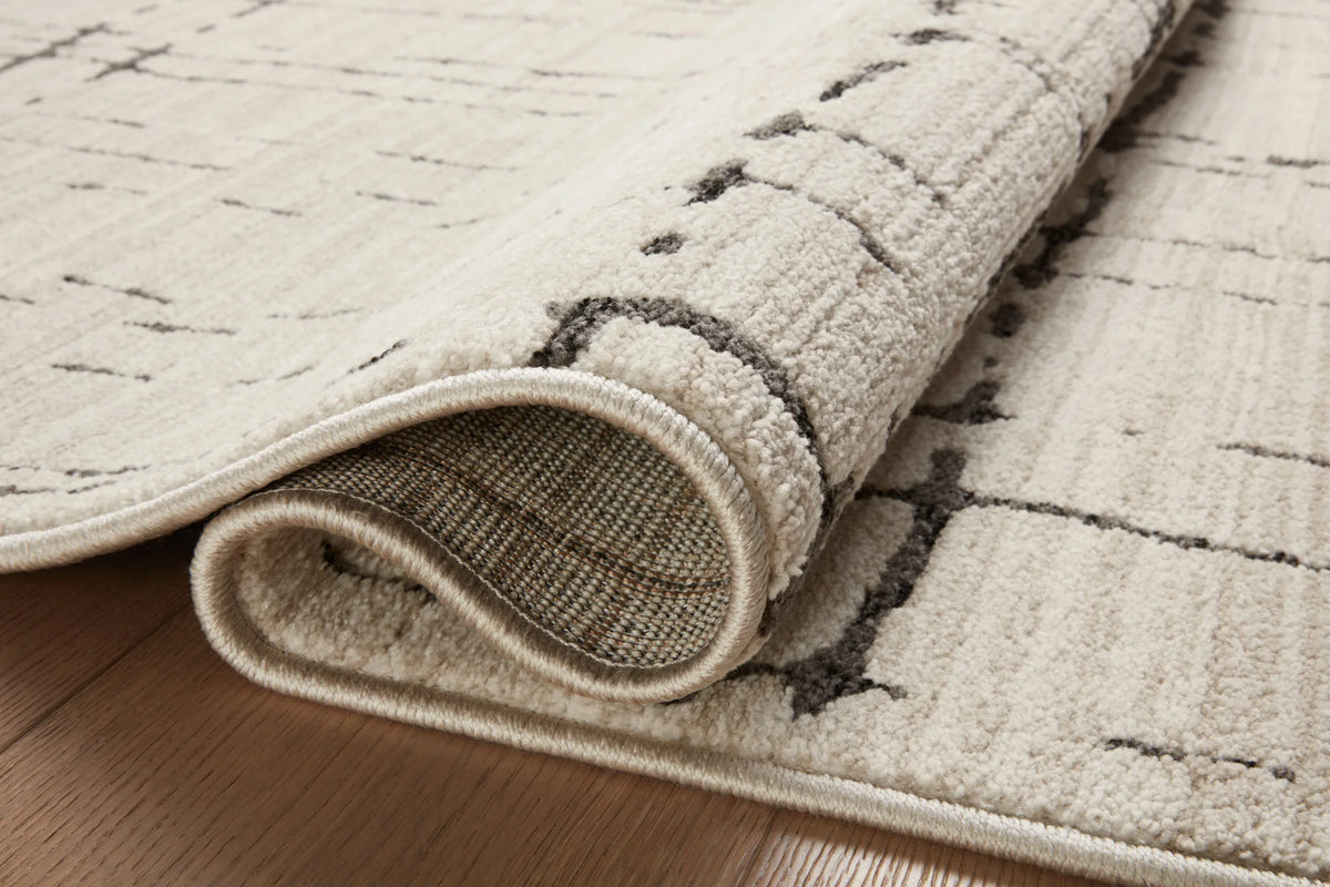 Sand area rug edge with dark gray lines and stitched binding, rolled view