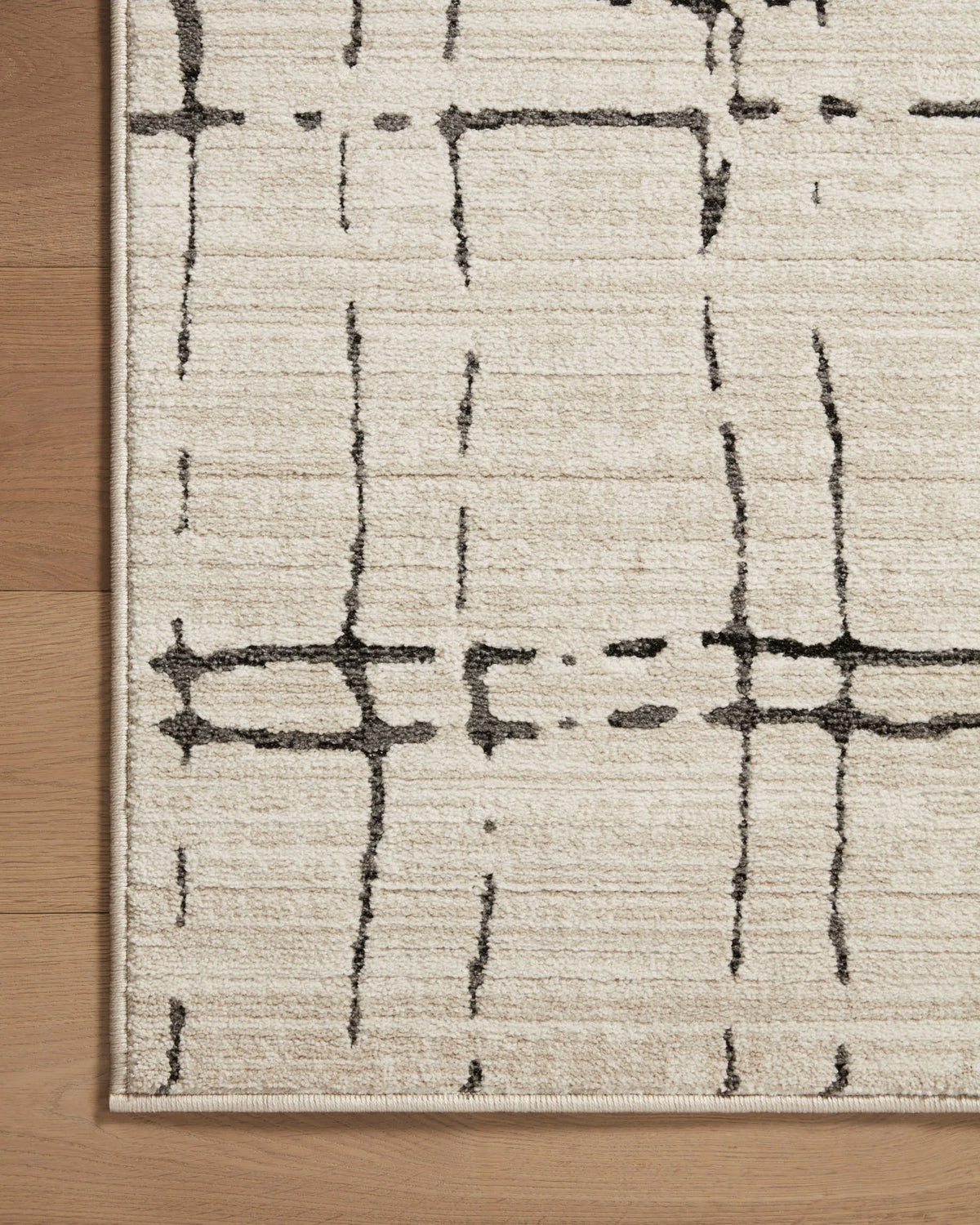 Corner of sand and dark gray area rug showing abstract intersecting line grid pattern.