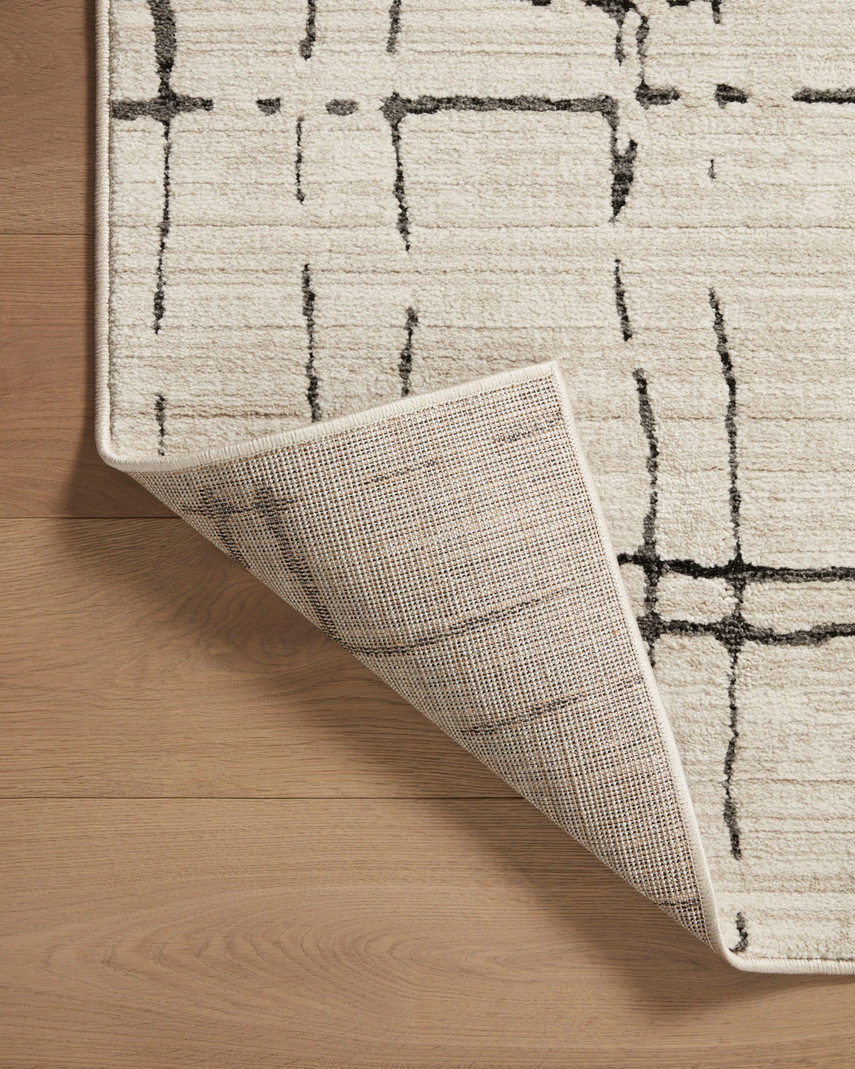 Sand rug corner with backing visible and dark geometric lines, close-up