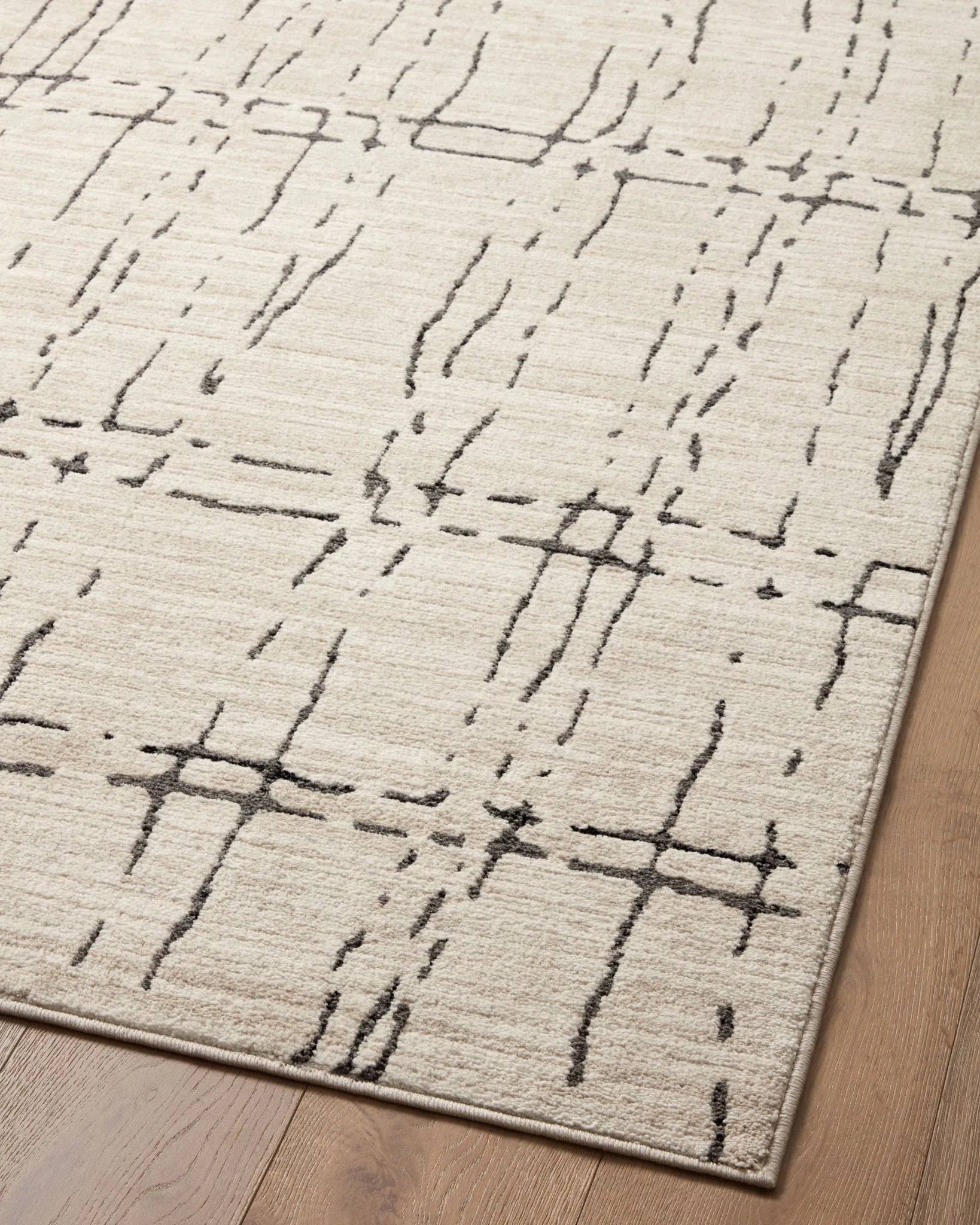 Close view of sand and dark gray area rug with abstract grid lines and visible border.