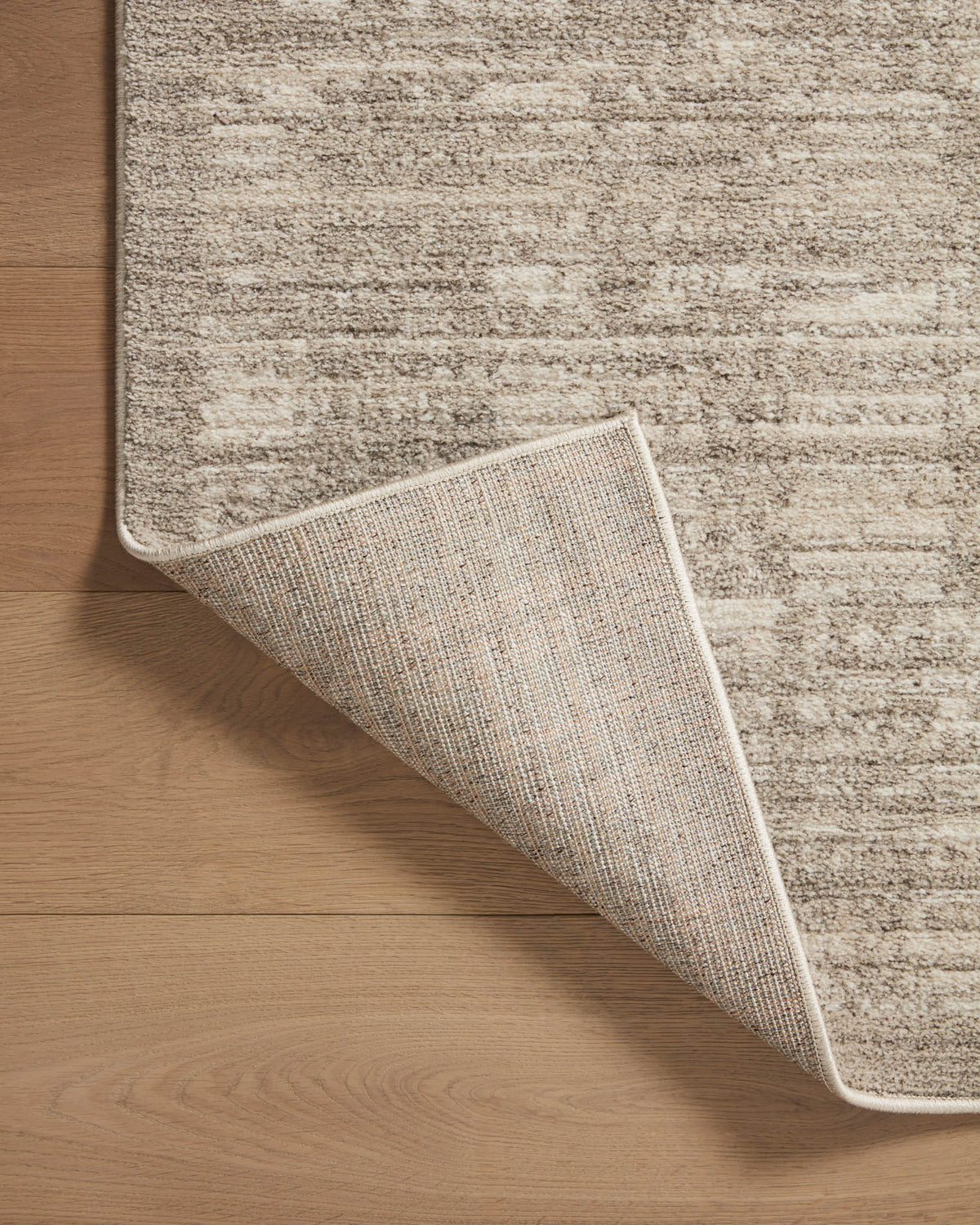 Sand and pebble area rug corner lifted to show woven backing and stitched edge