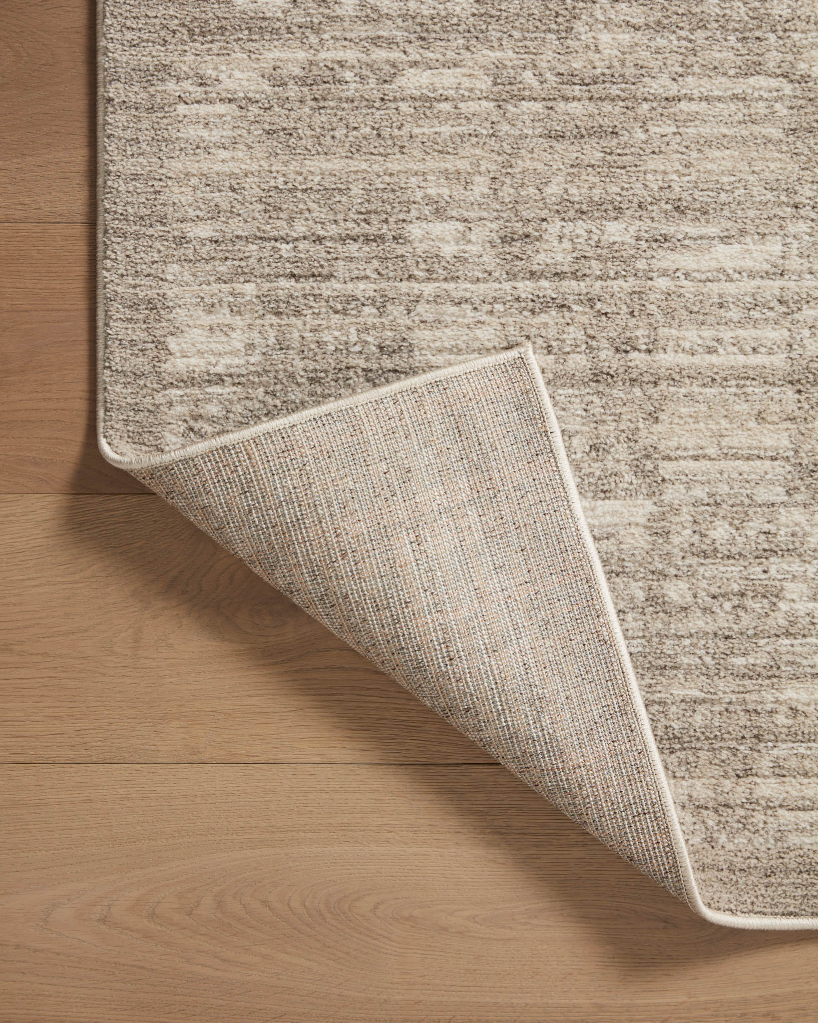Close-up of beige and gray area rug edge with woven border on backing