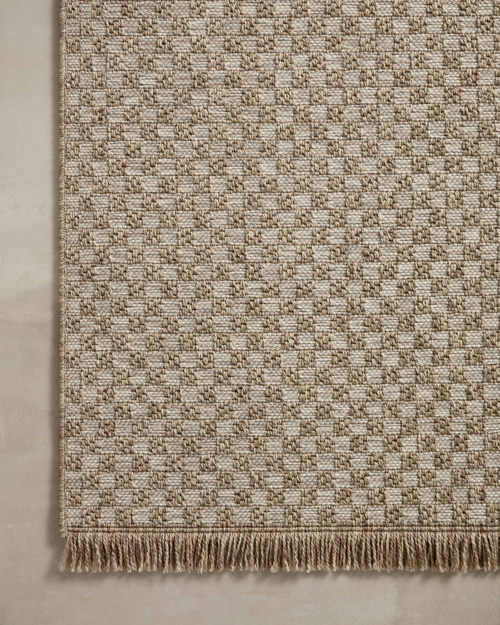 Natural beige area rug with allover lattice weave and fringed border, tight close-up.