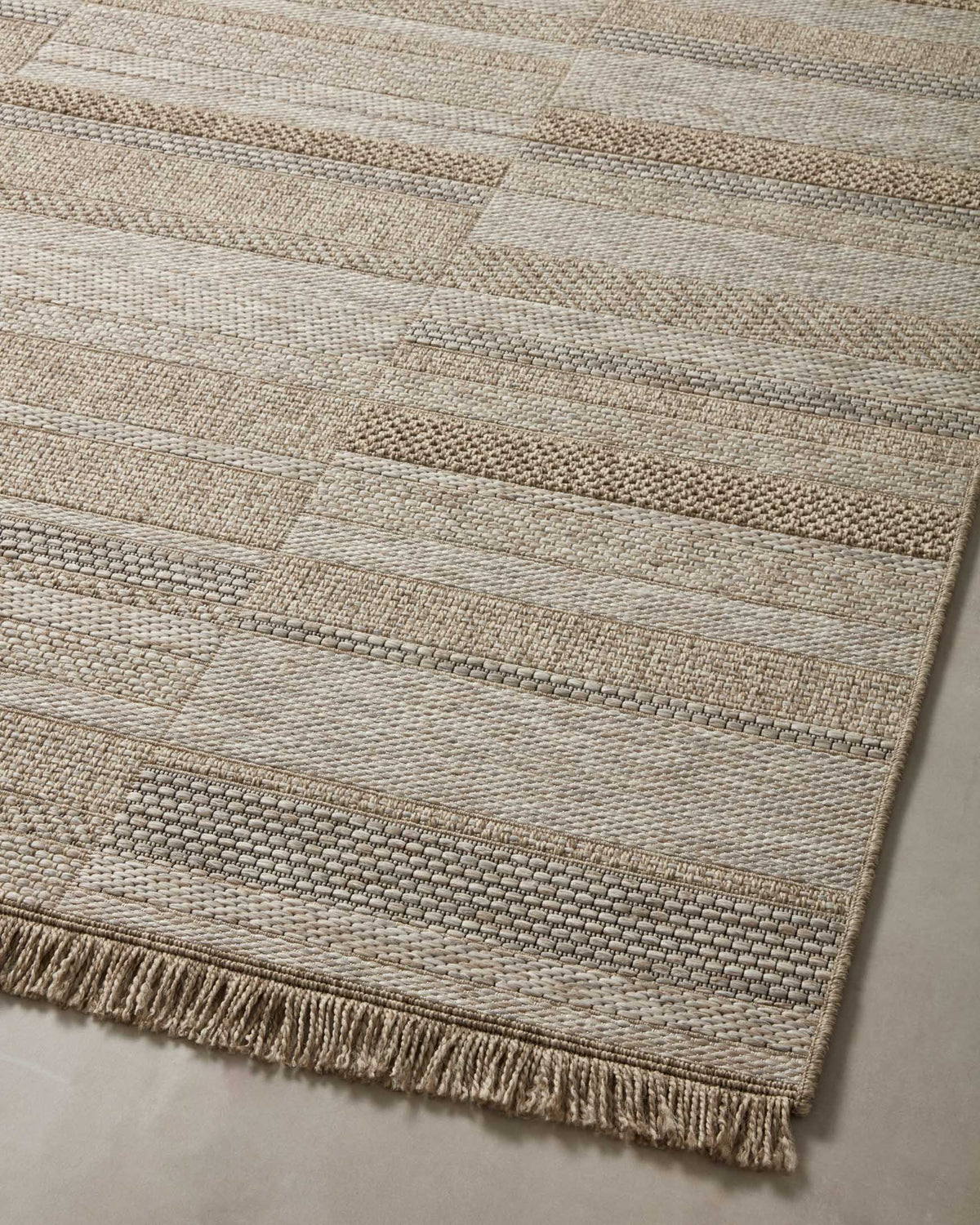 Natural woven rug top view with patchwork rectangles in light and tan tones and fringe