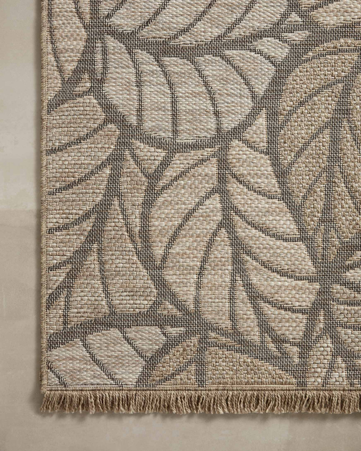 Natural area rug corner with gray botanical leaf motif and textured fringe