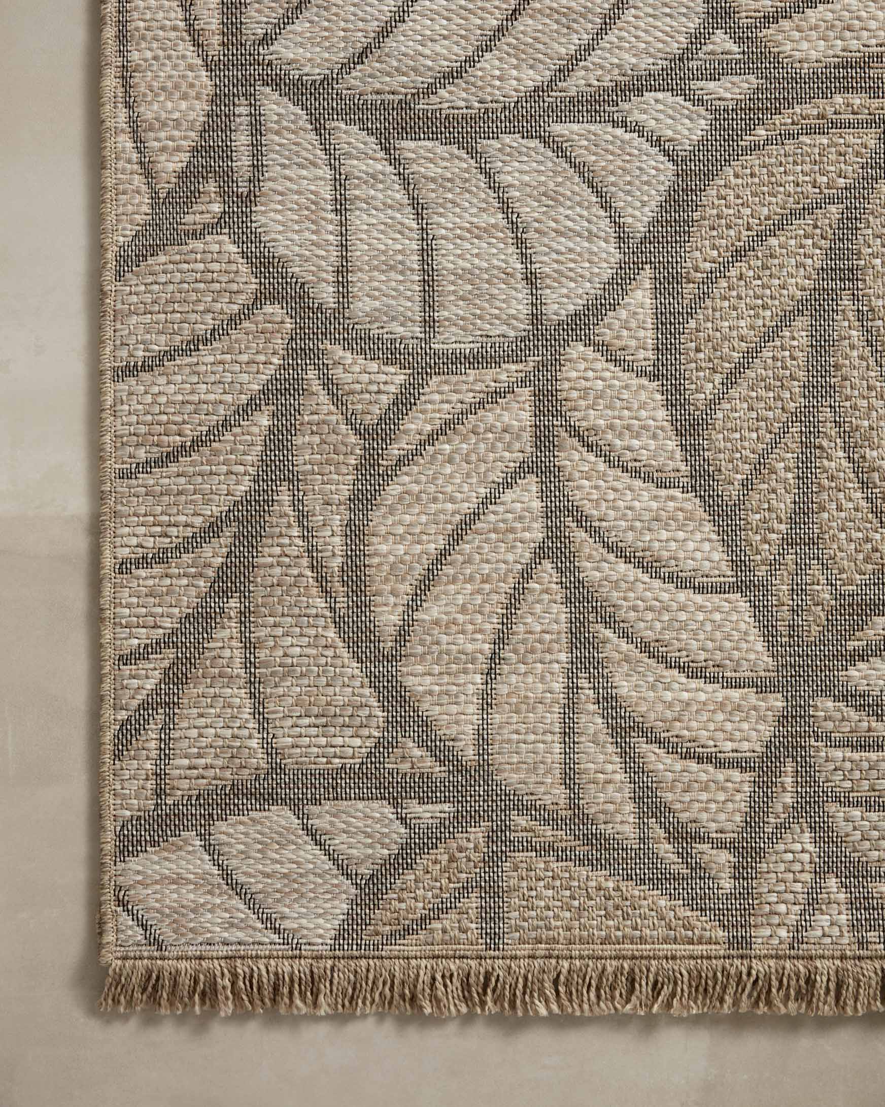 Close-up natural leaf-pattern rug corner with fringed edge and woven texture.