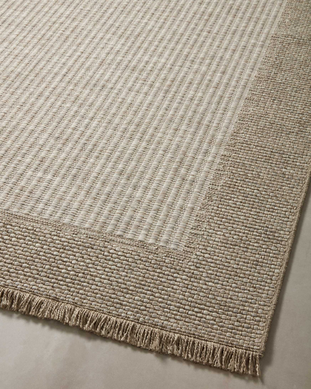 Natural flatweave area rug with light checker pattern and darker border, fringed edge