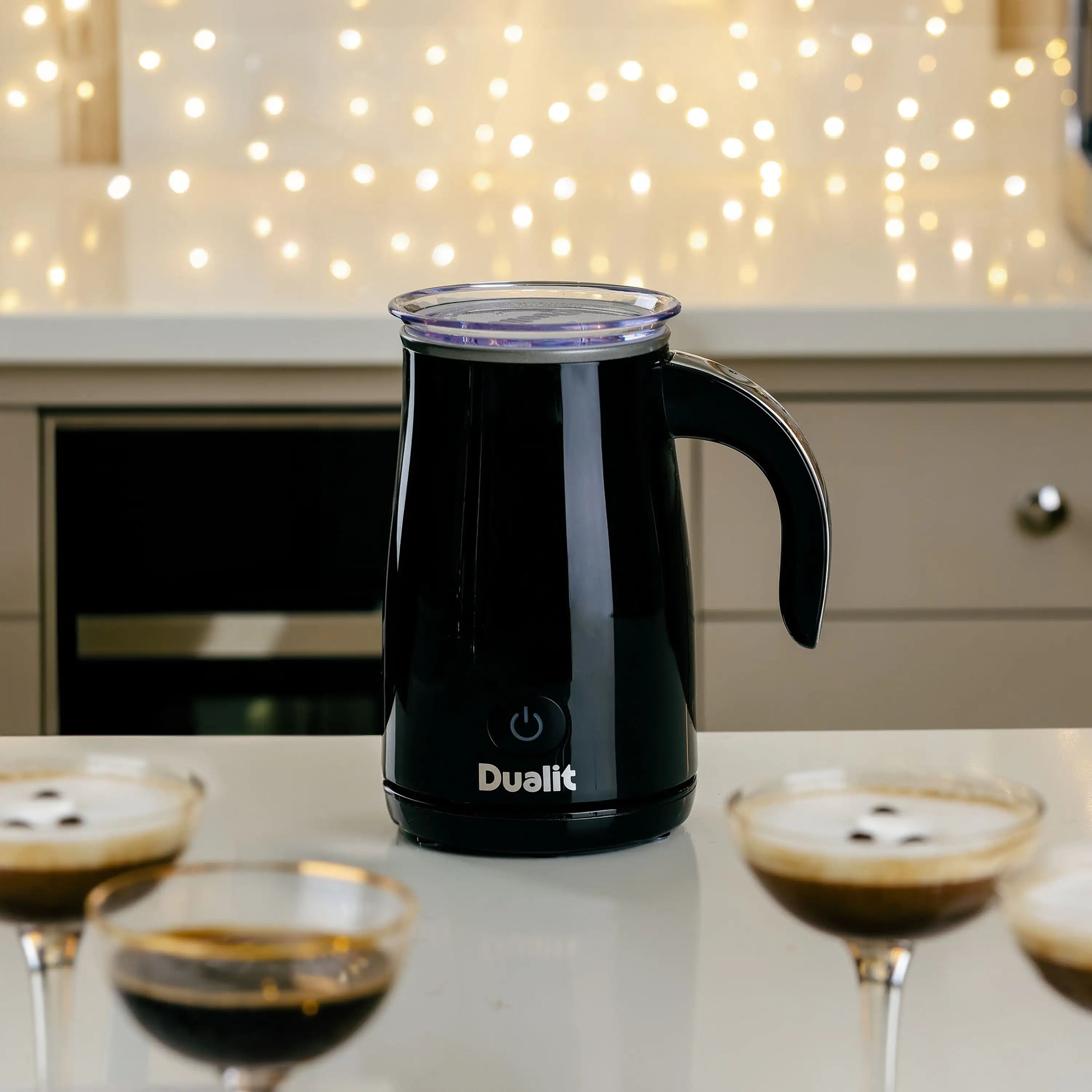 Black electric milk frother on countertop with lid and side handle
