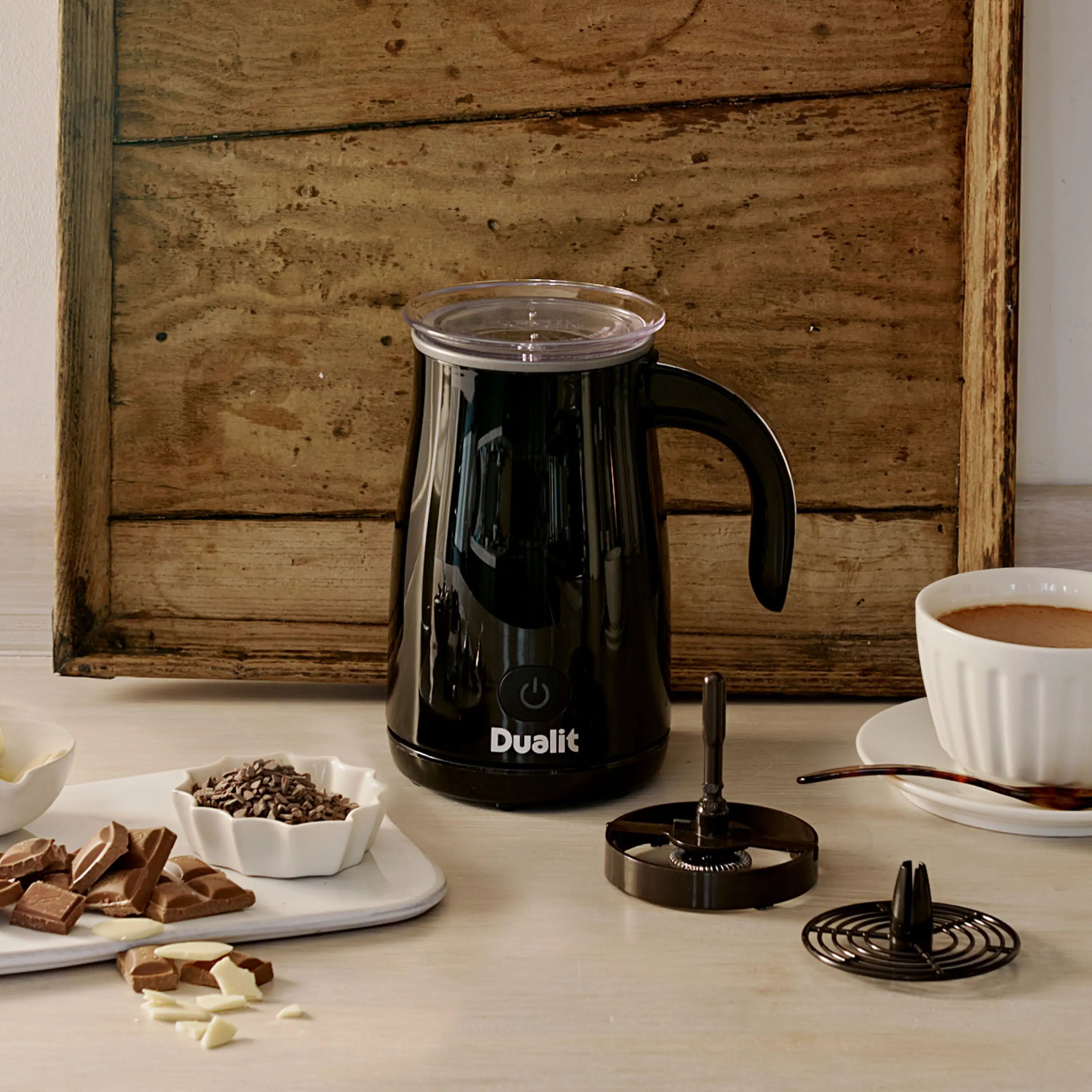 Black Dualit hot chocolate maker on countertop with frothing lid and stand