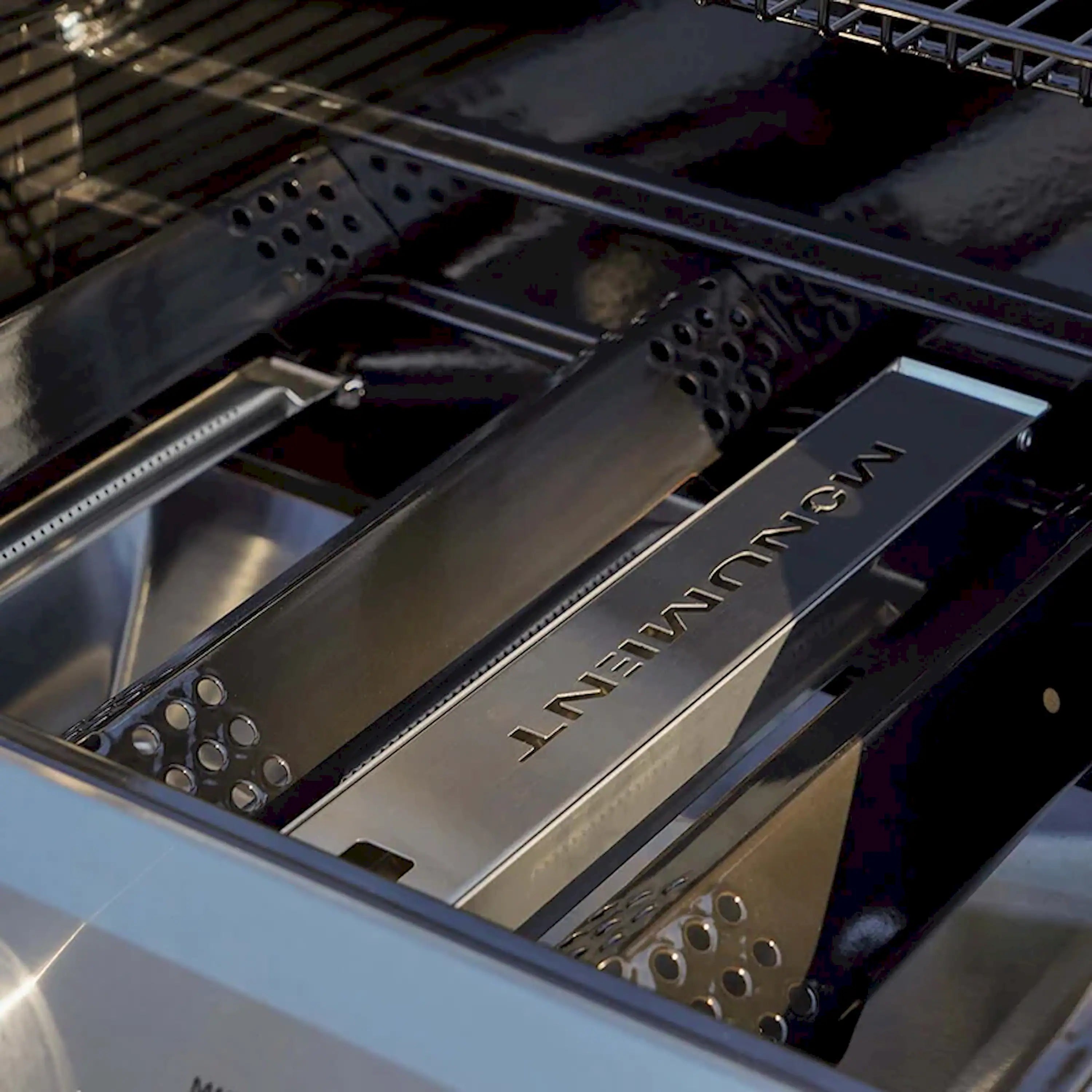 Stainless smoker box tray with MONUMENT logo, vent holes, and perforated ends