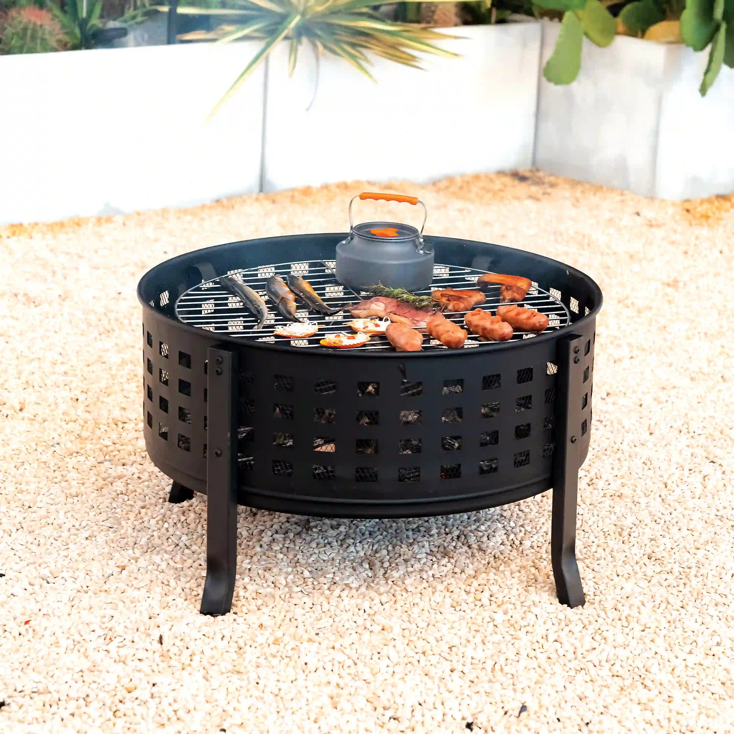 Black round fire pit grill with cooked food on the grate under a mesh spark screen