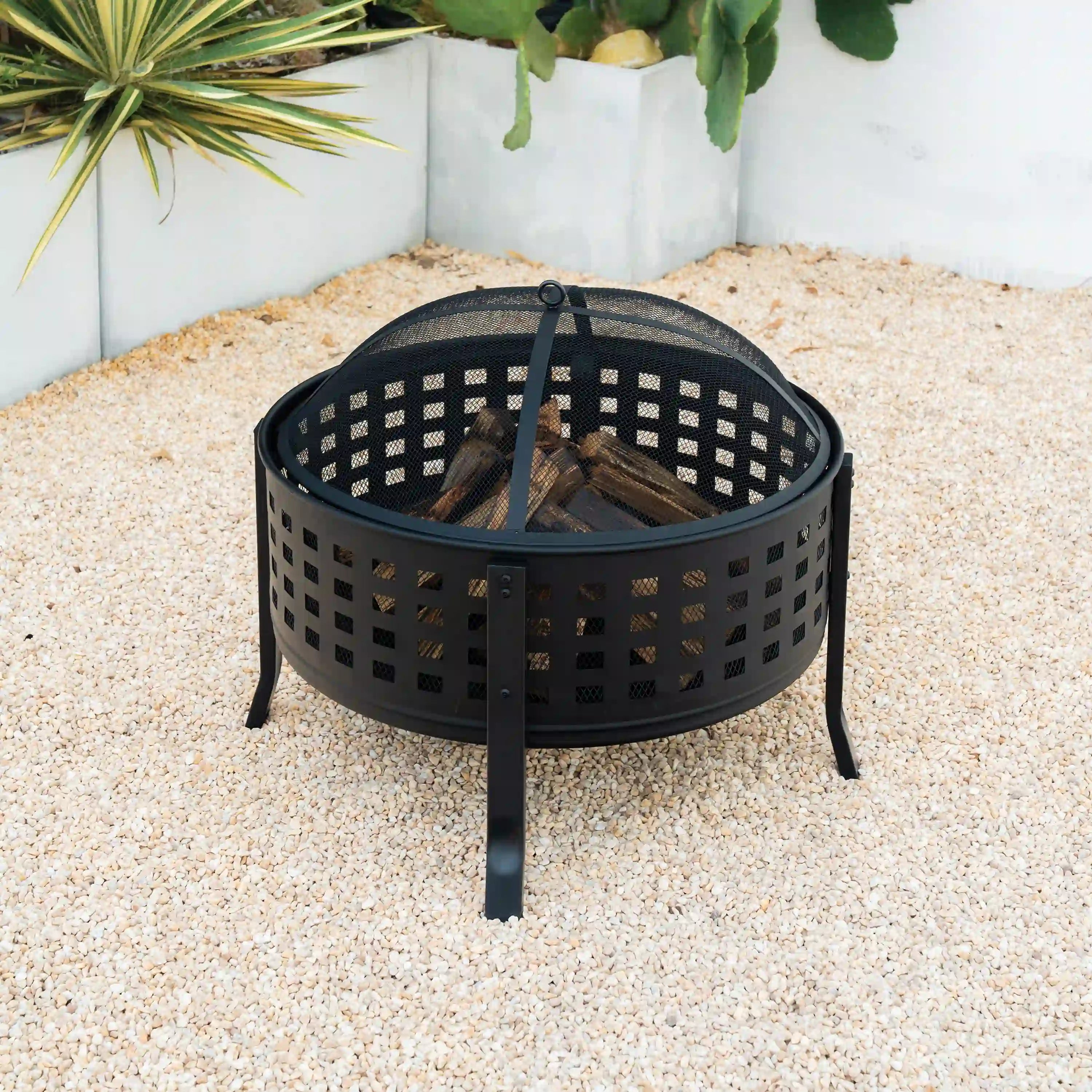 Black round fire pit with mesh spark screen and stacked firewood inside