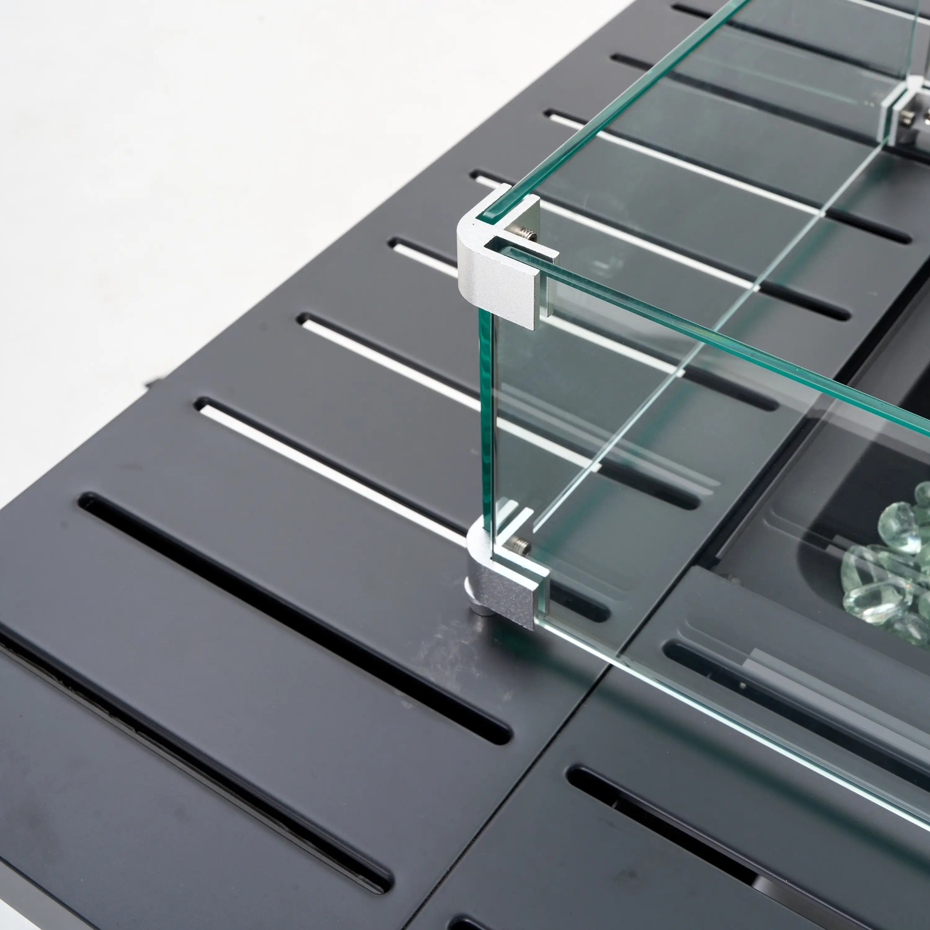 Glass wind guard with corner frame on dark fire pit burner tray