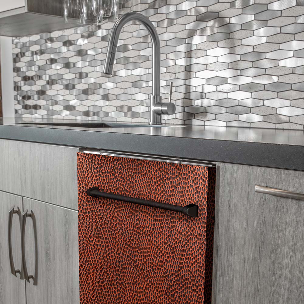 Dishwasher hammered copper front panel with recessed handle near a faucet.