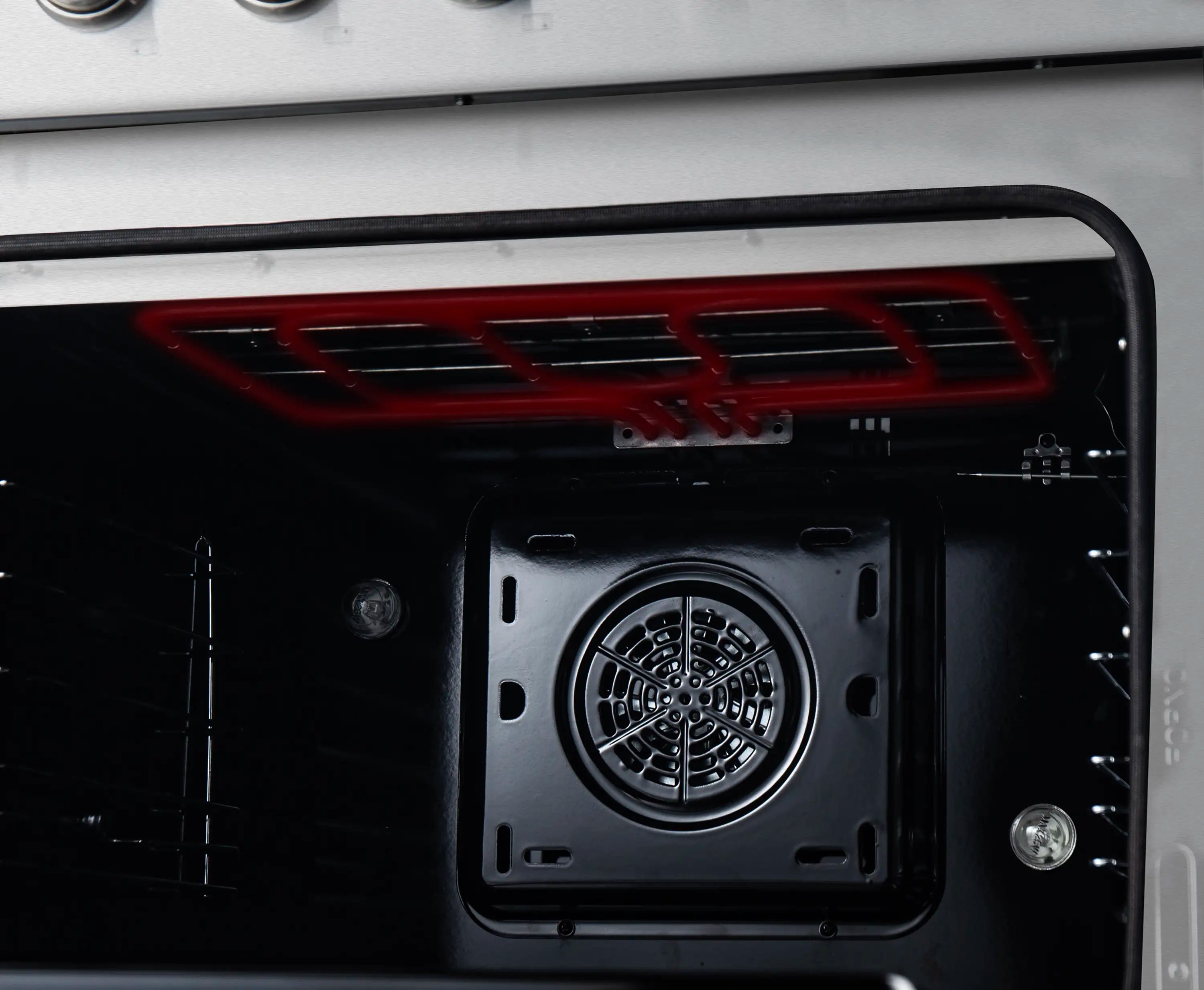 Dual fuel range oven interior with red heating element glowing above fan housing.