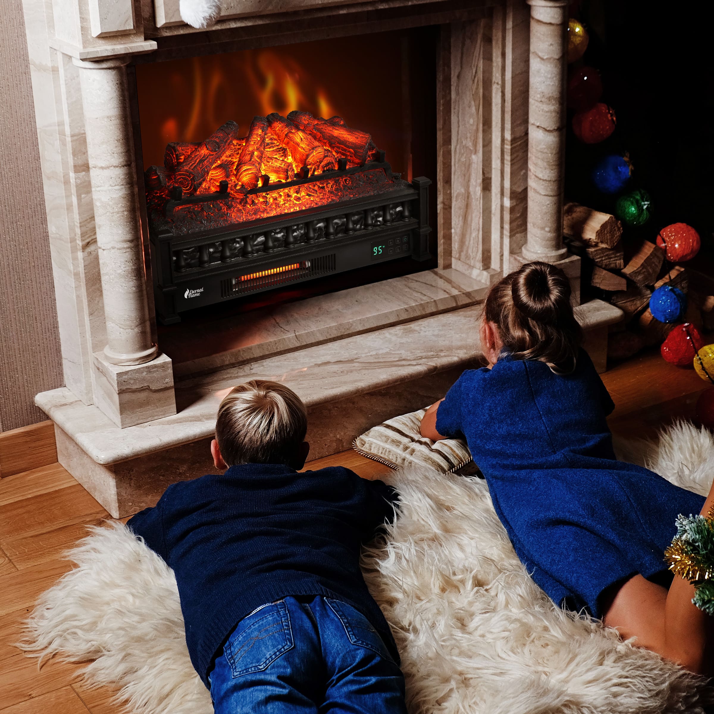 Electric fireplace log set with orange flames, two children sitting facing the unit