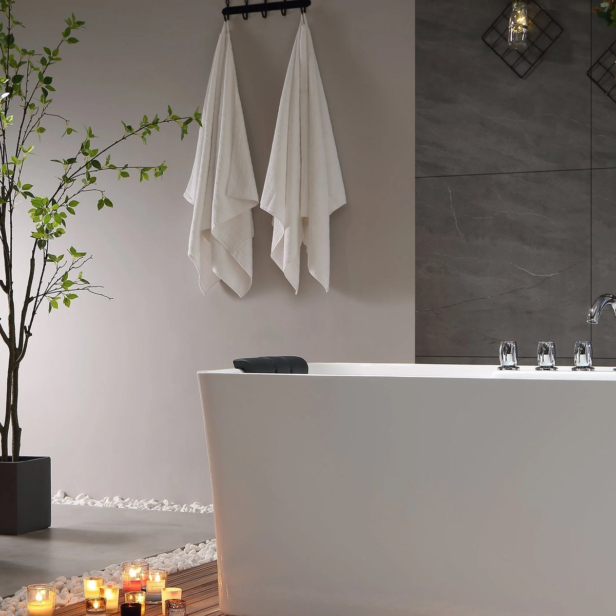 White freestanding acrylic bathtub with black headrest and chrome faucet, side-front view.
