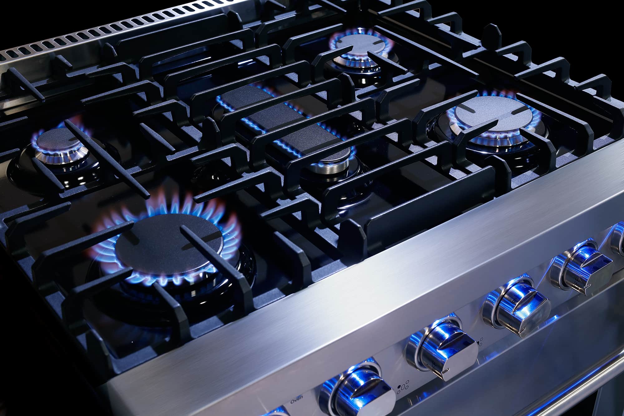 Gas cooktop burner with visible blue flames on stainless steel surface