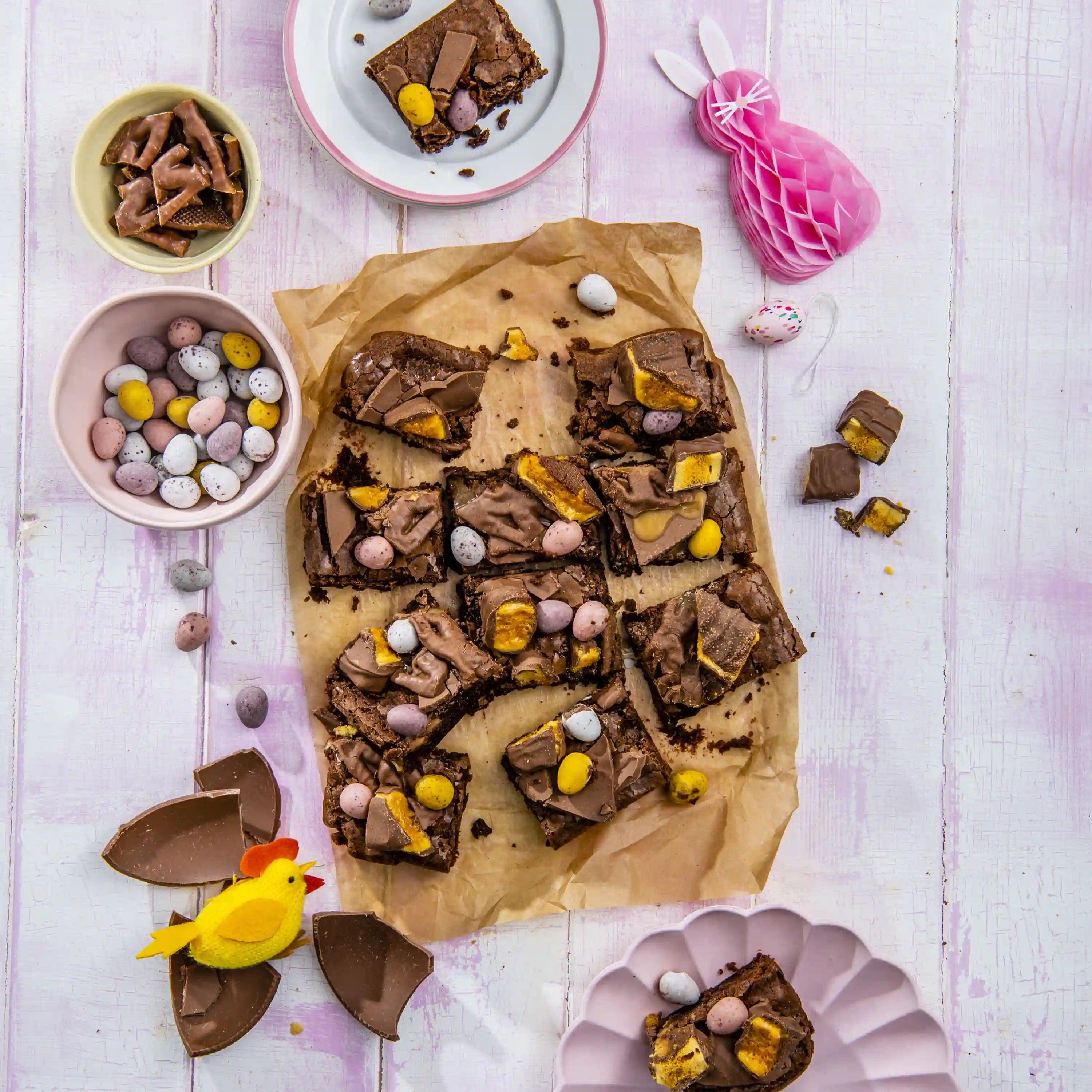 Baked chocolate brownie pieces on parchment with pastel easter eggs