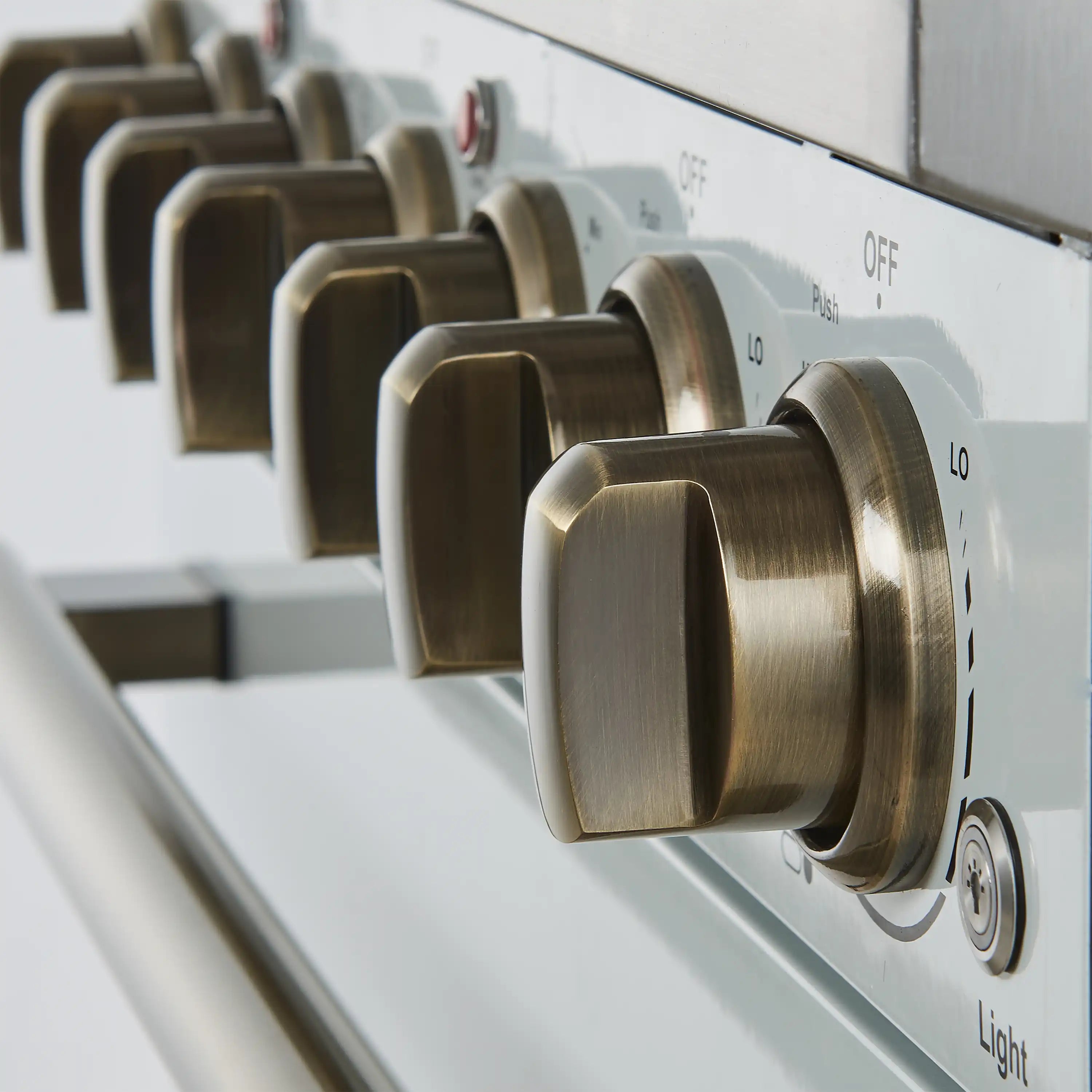 Brass control knobs on a white electric range with labeled settings