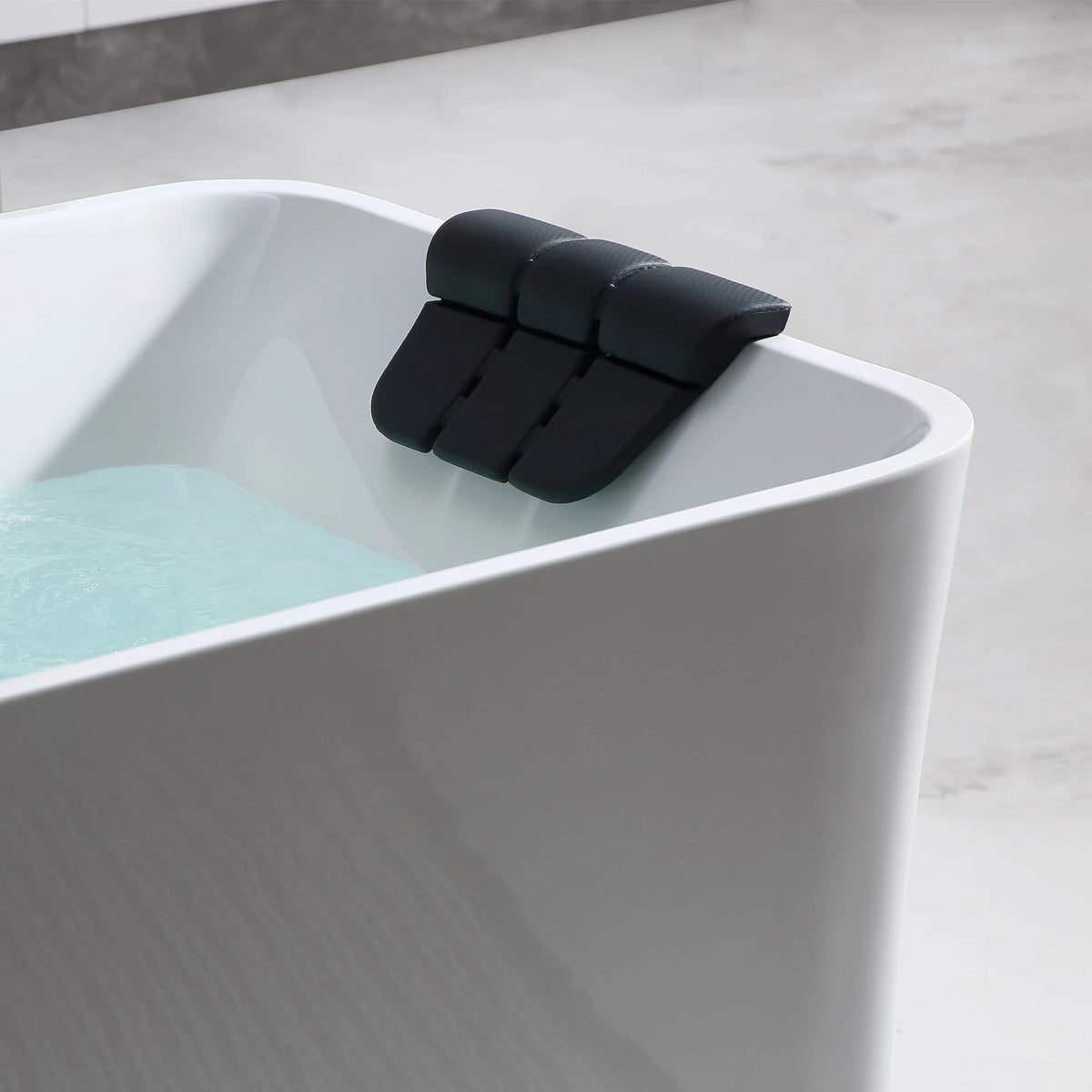 Close-up of black headrest on white whirlpool bathtub rim with light blue water