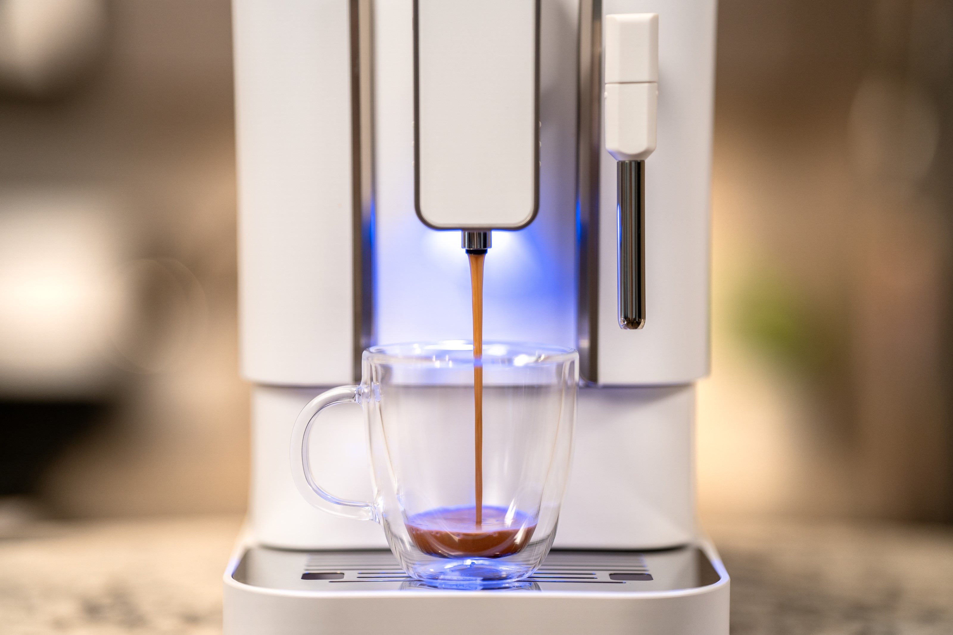 Close-up bean to cup espresso machine spout pouring into clear cup with blue light