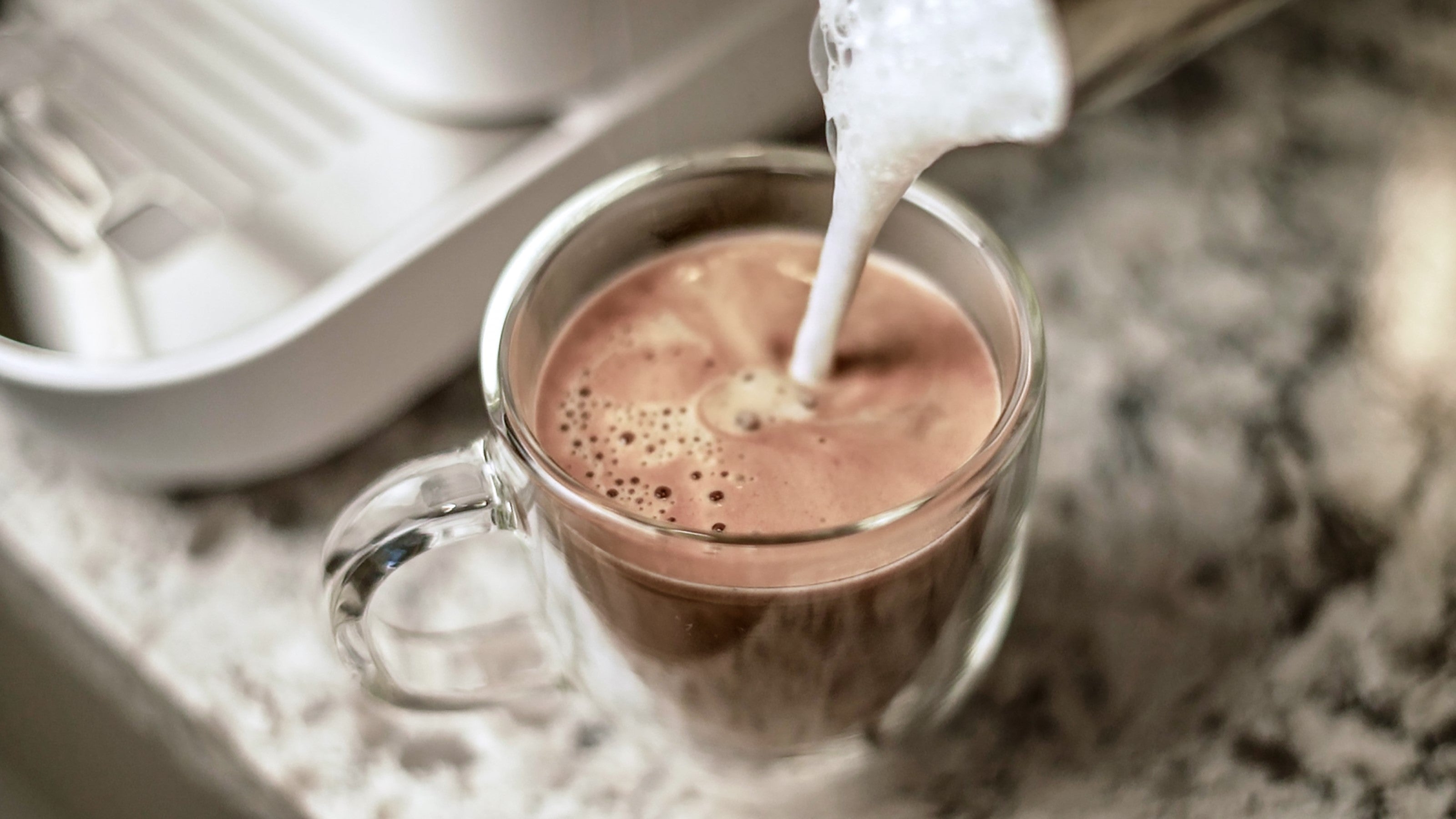 Clear glass cup under spout with frothy espresso in a diamond white machine