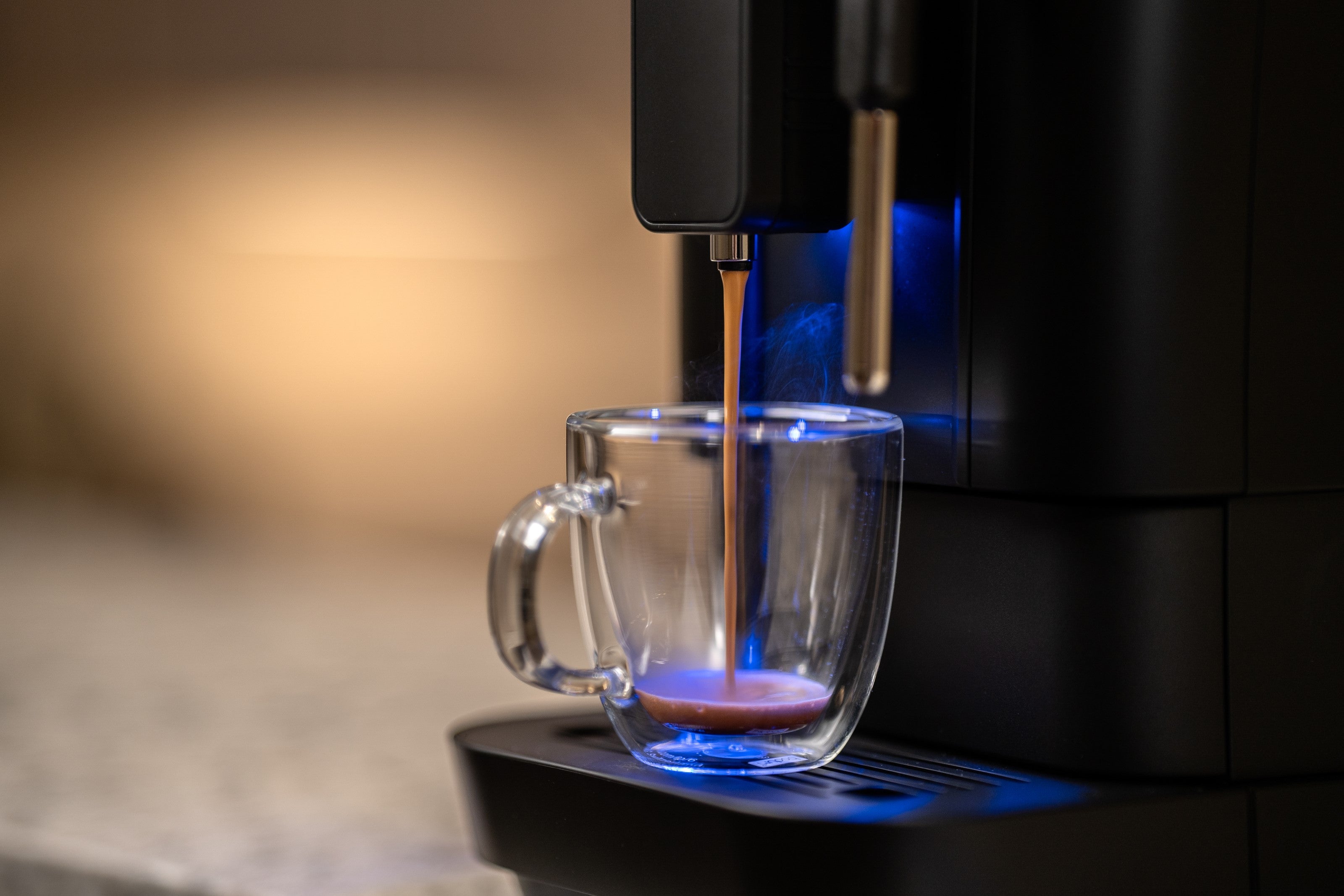 Black fully automatic bean-to-cup espresso machine pouring into clear cup