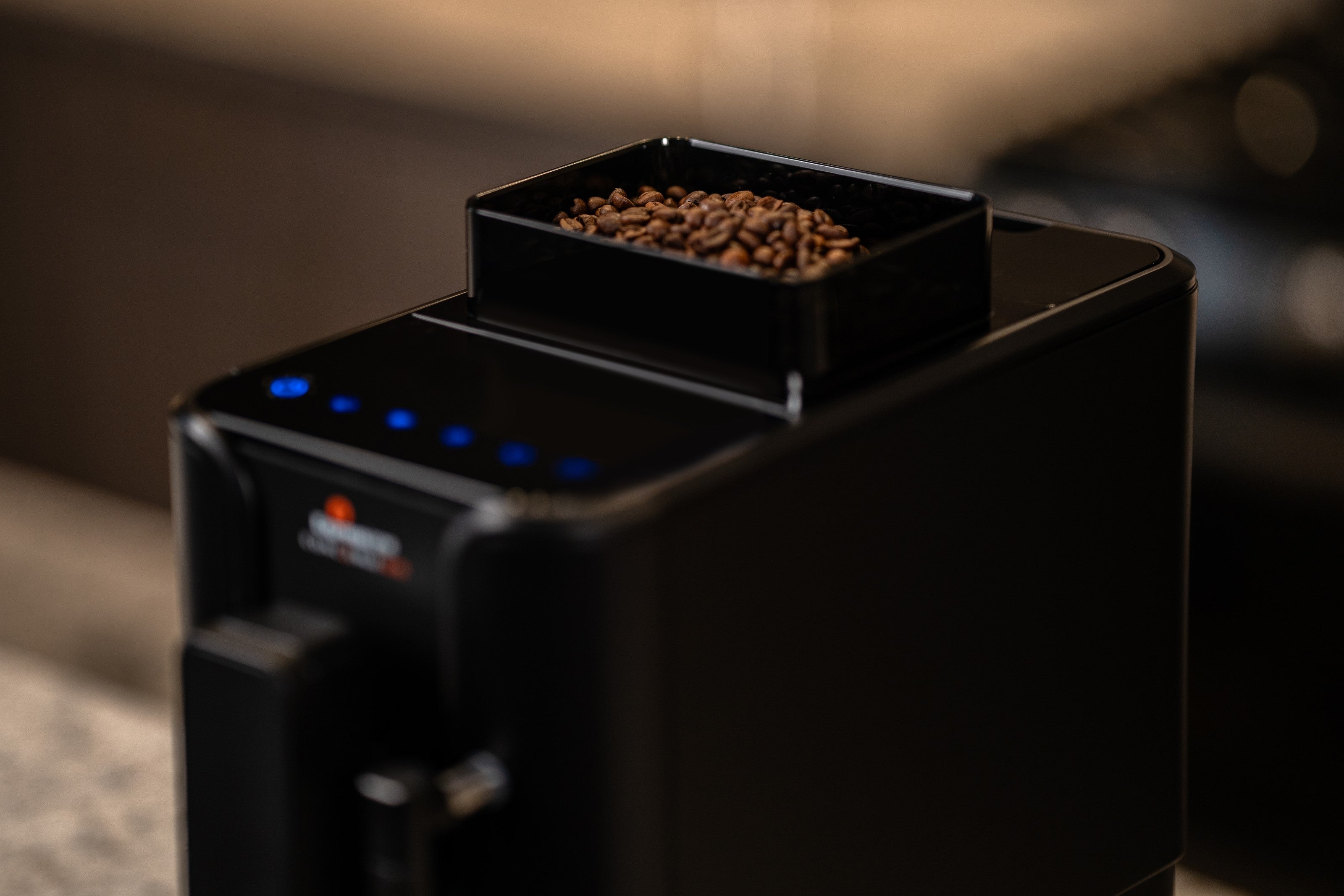 Black bean hopper open above espresso machine, coffee beans inside