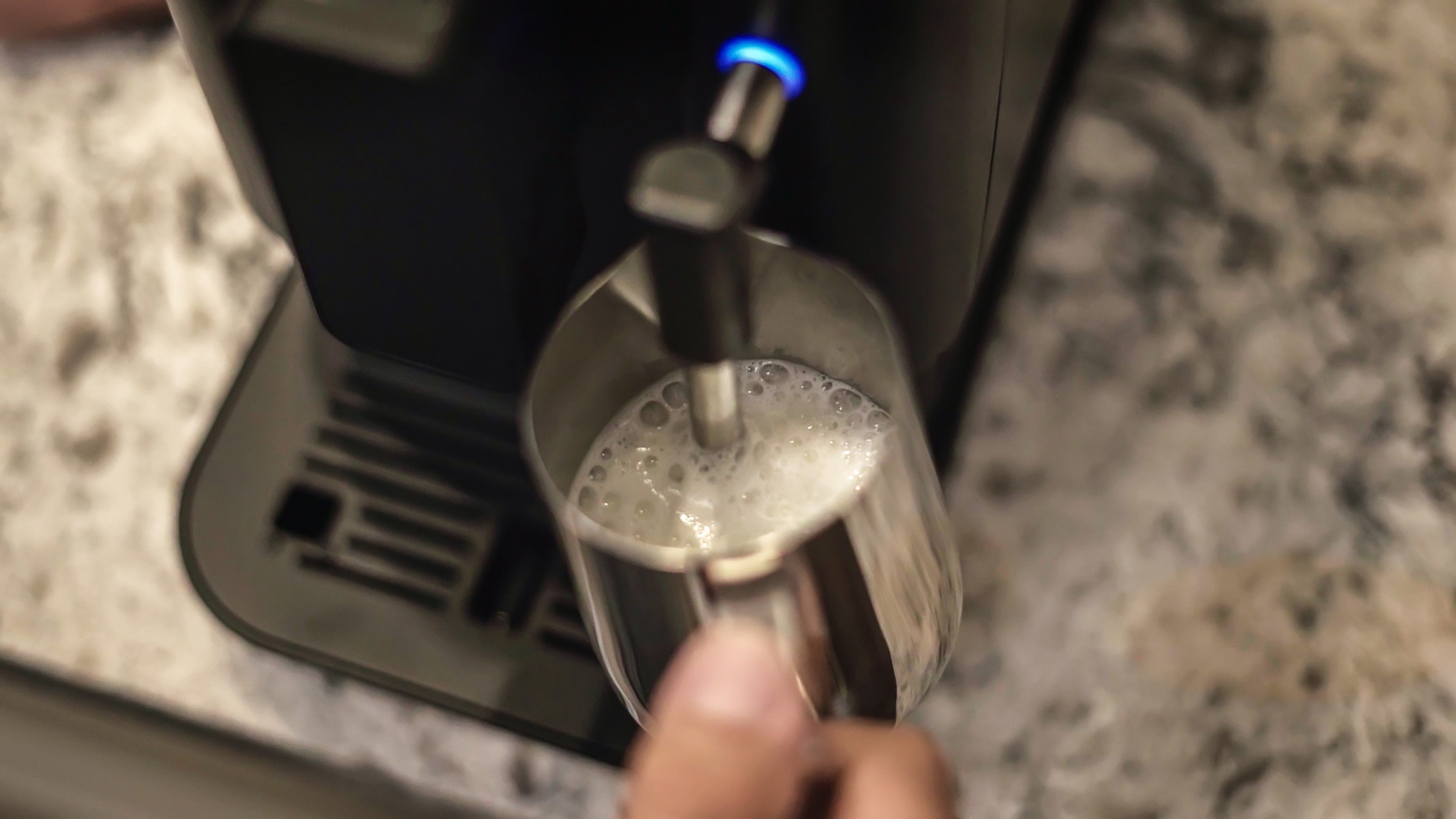 Steam wand frothing milk into clear metal cup on drip tray