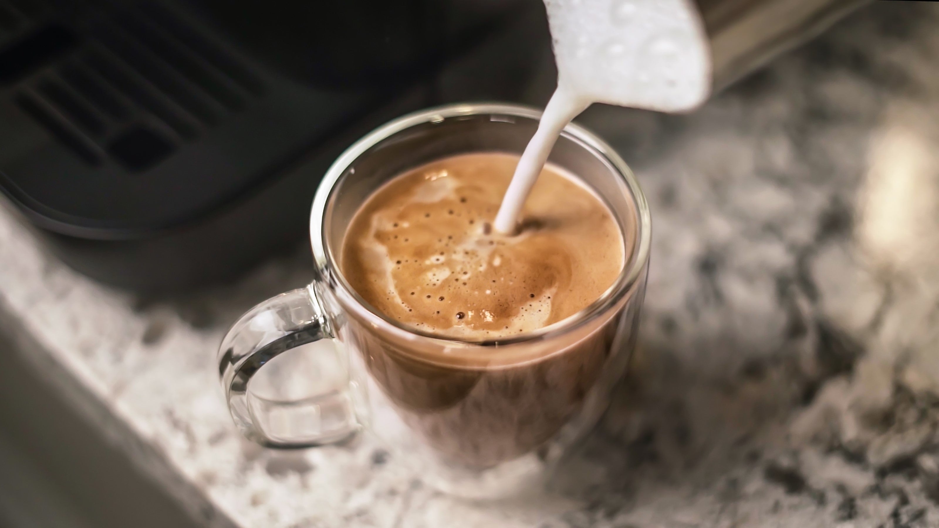 Creamy latte foam pouring into glass mug from espresso spout