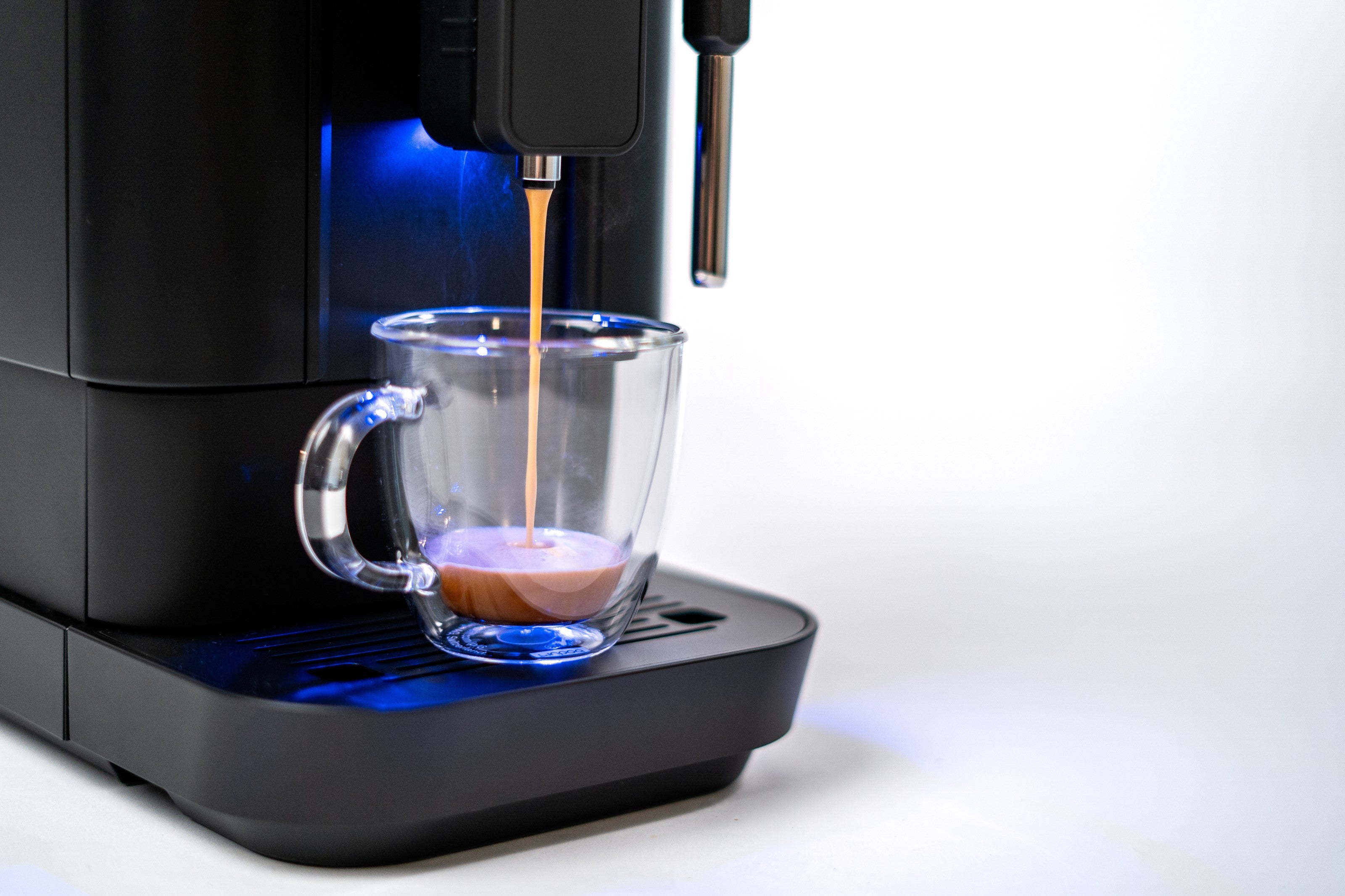 Close view of black espresso machine spout pouring into clear cup