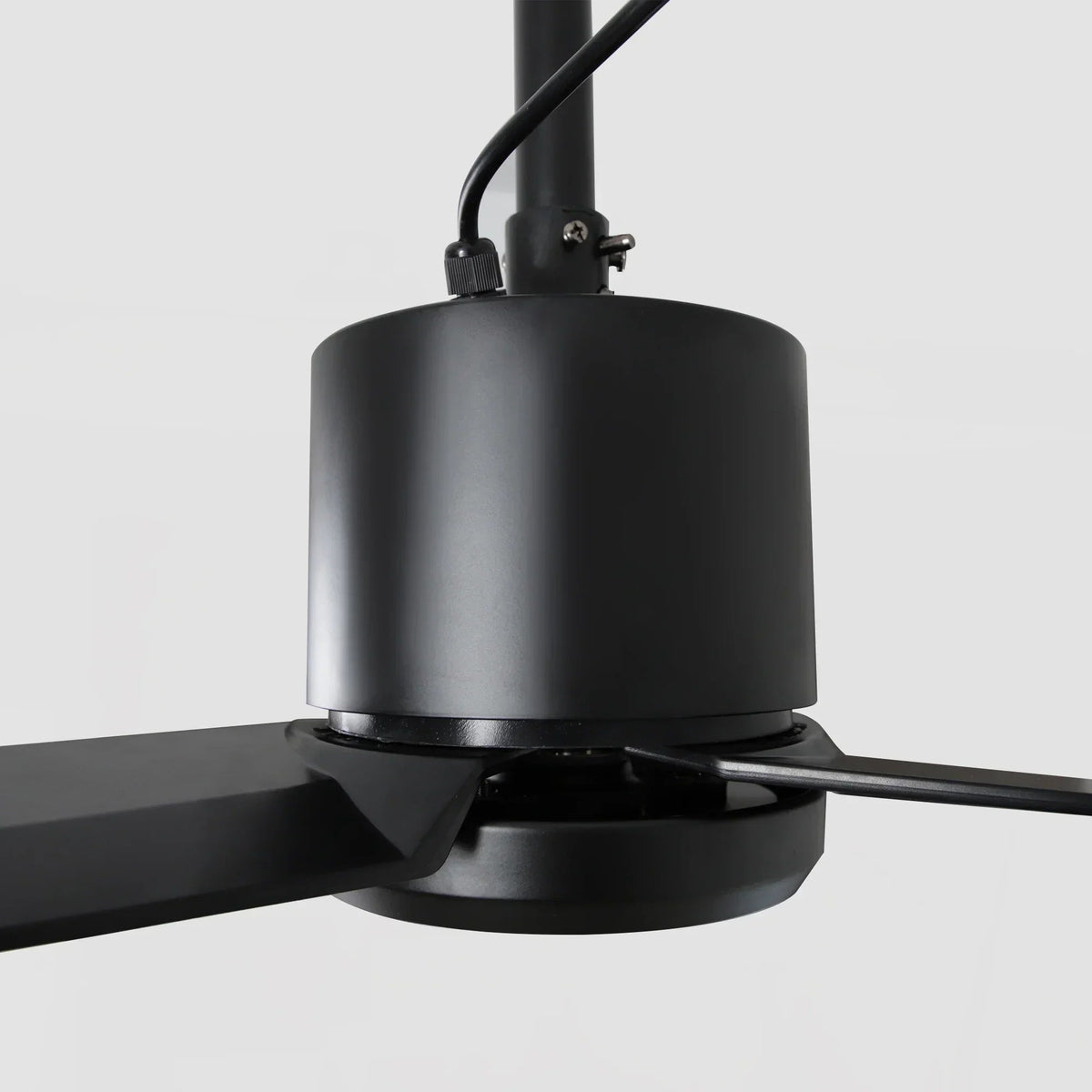 Black ceiling fan motor housing with downrod connection and three-blade base