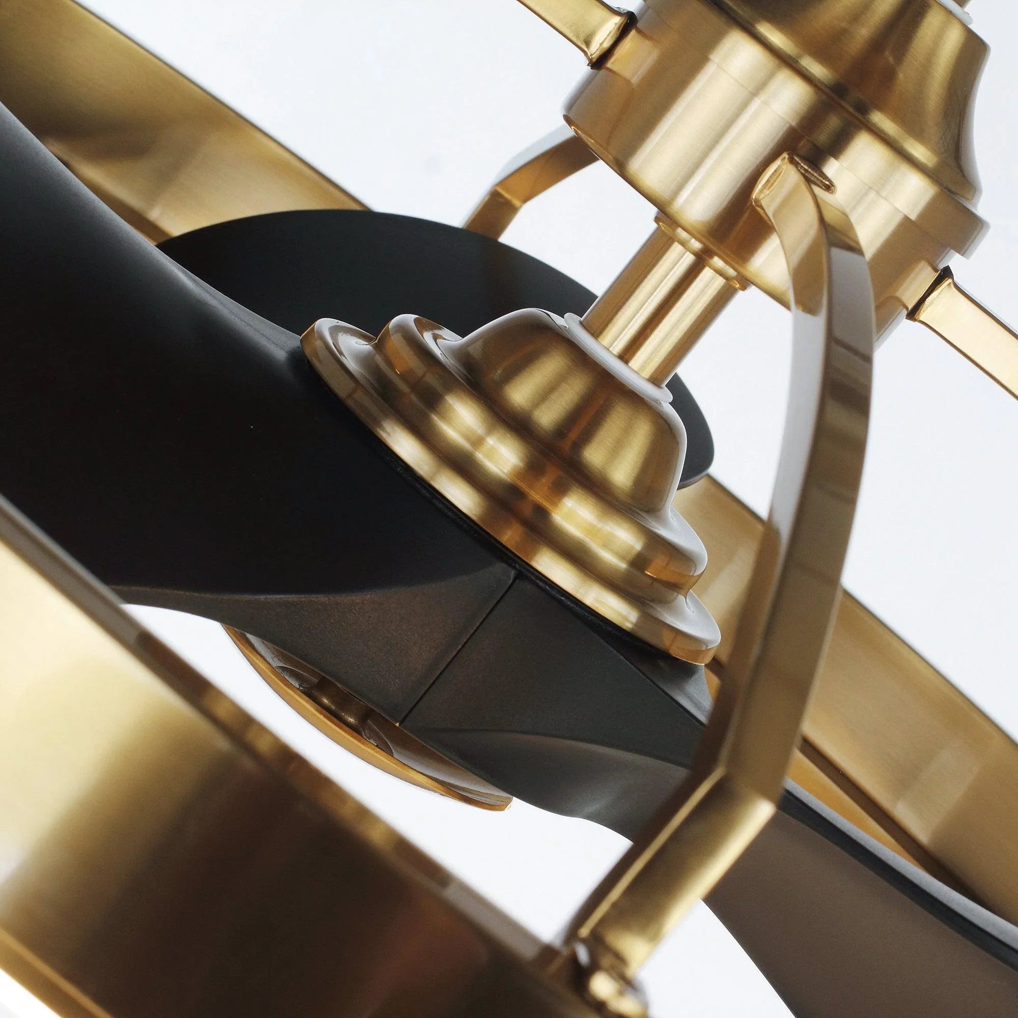 Close-up of golden ceiling fan downrod and black blades near light ring