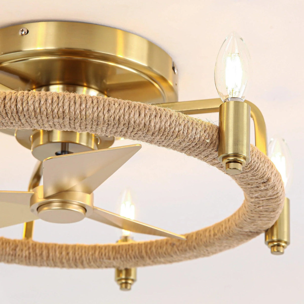 Close-up of golden flush mount fan arm, rope-wrapped ring, and candle-style light socket