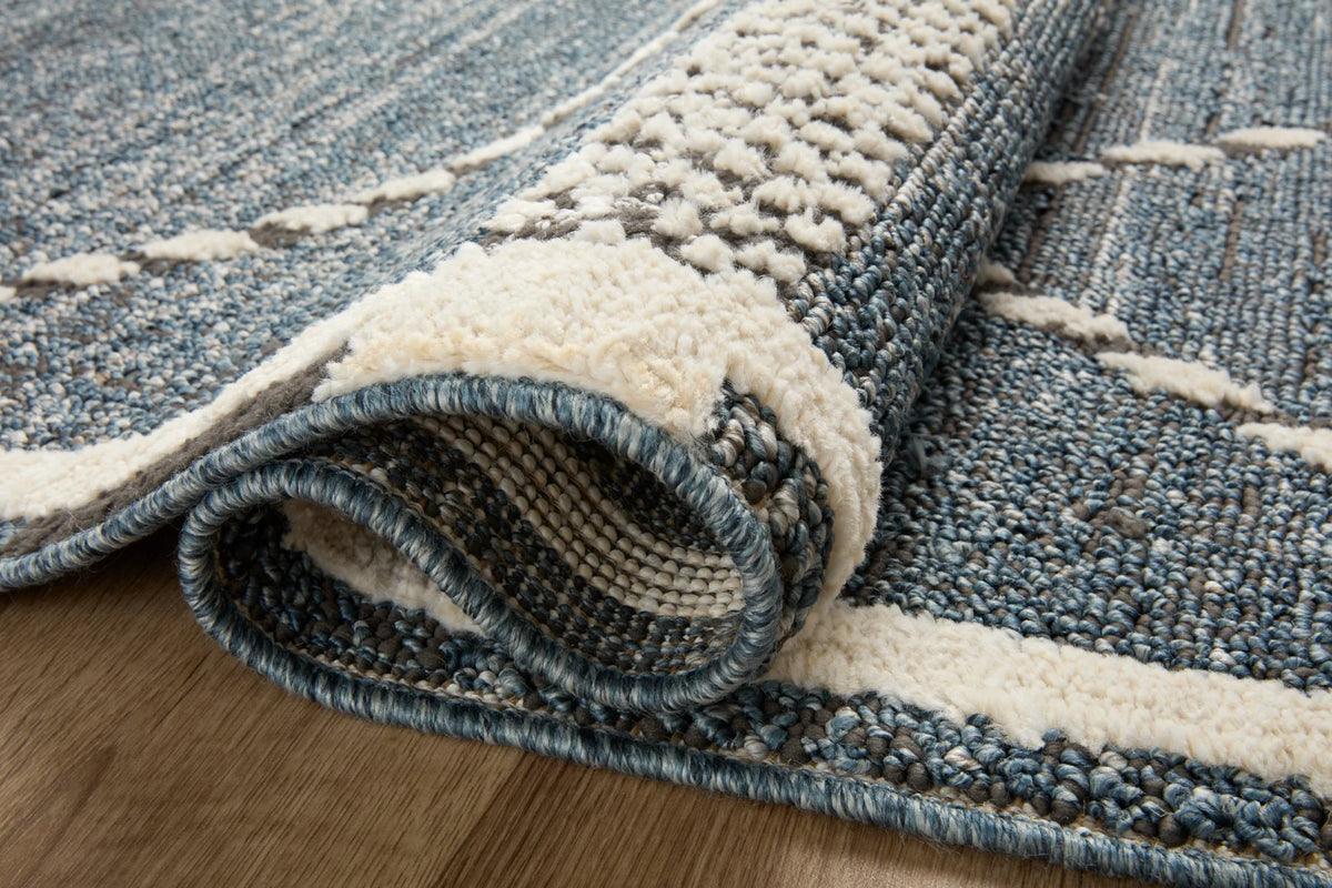Rolled edge detail of denim blue and cream geometric area rug with textured pile