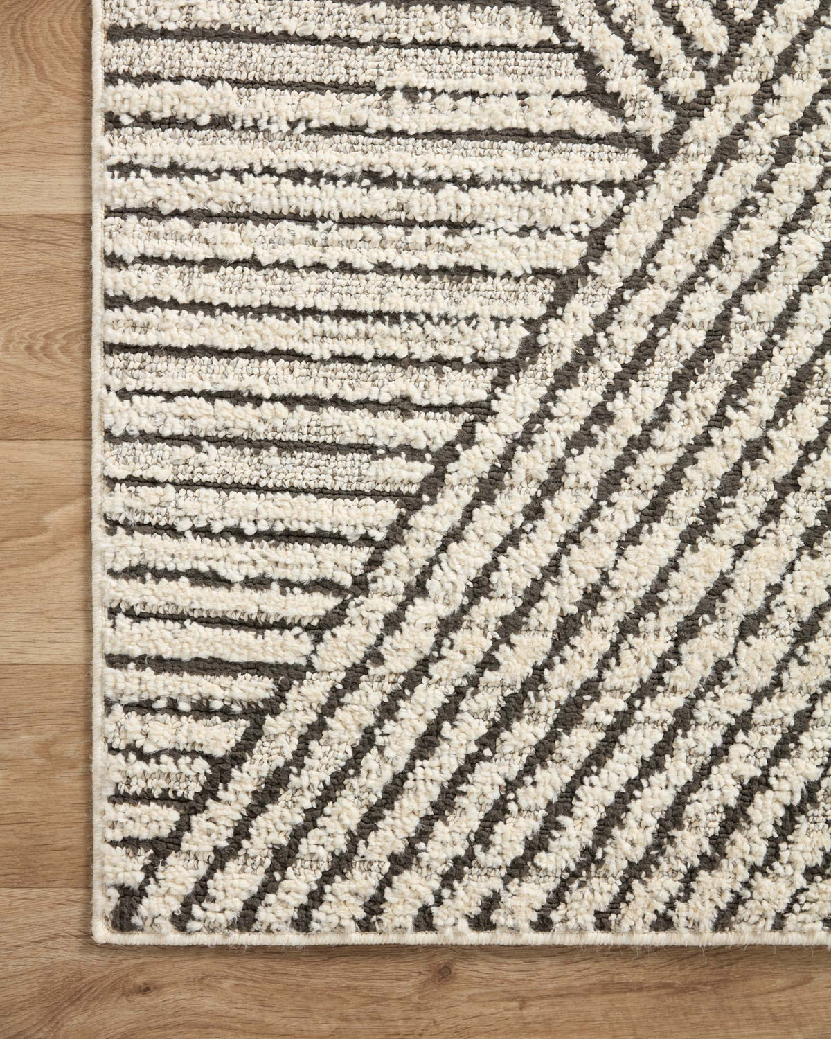Corner view of ivory and charcoal area rug with stacked stripes and geometric bands.