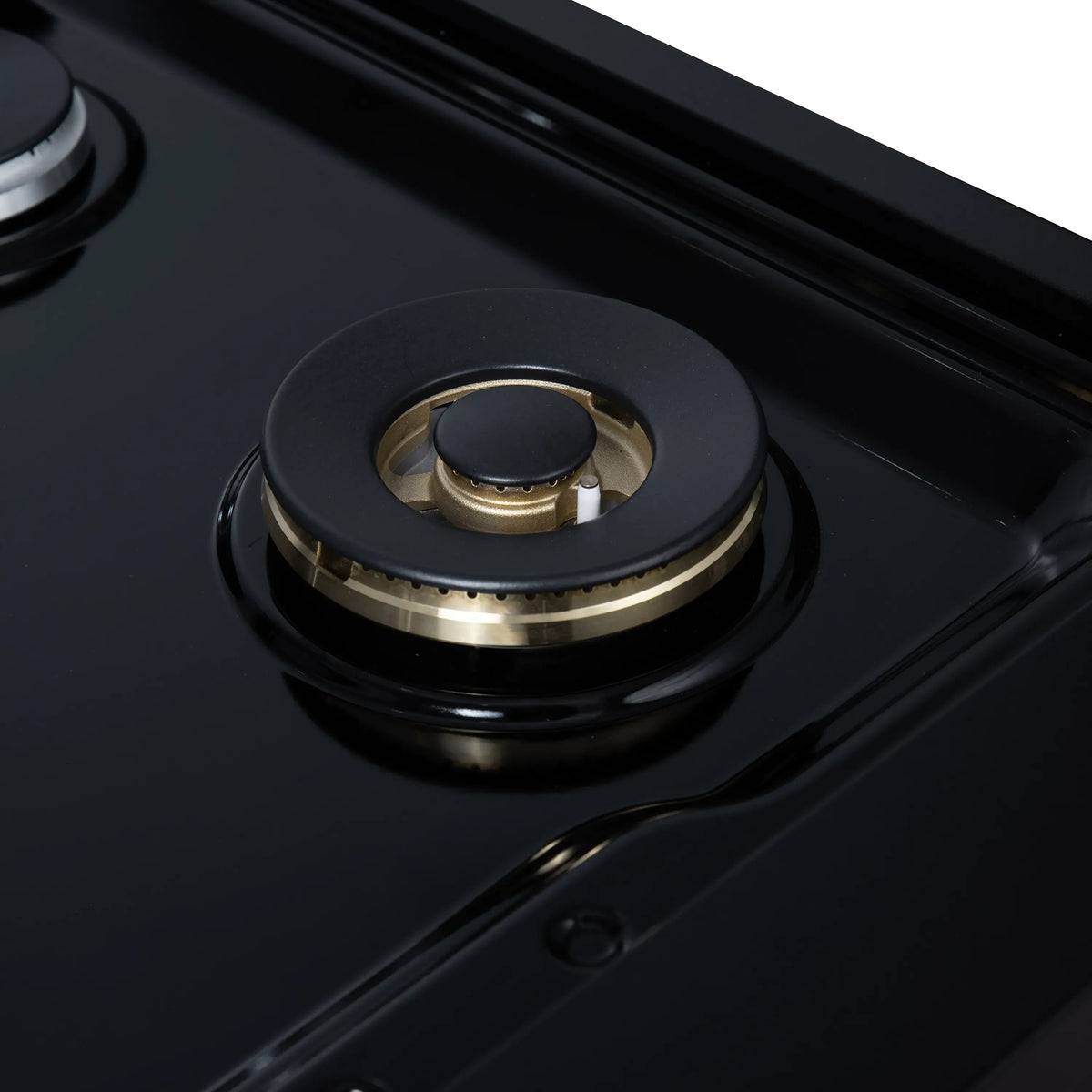 Black gas cooktop burner with round cap and brass center, unlit, close-up