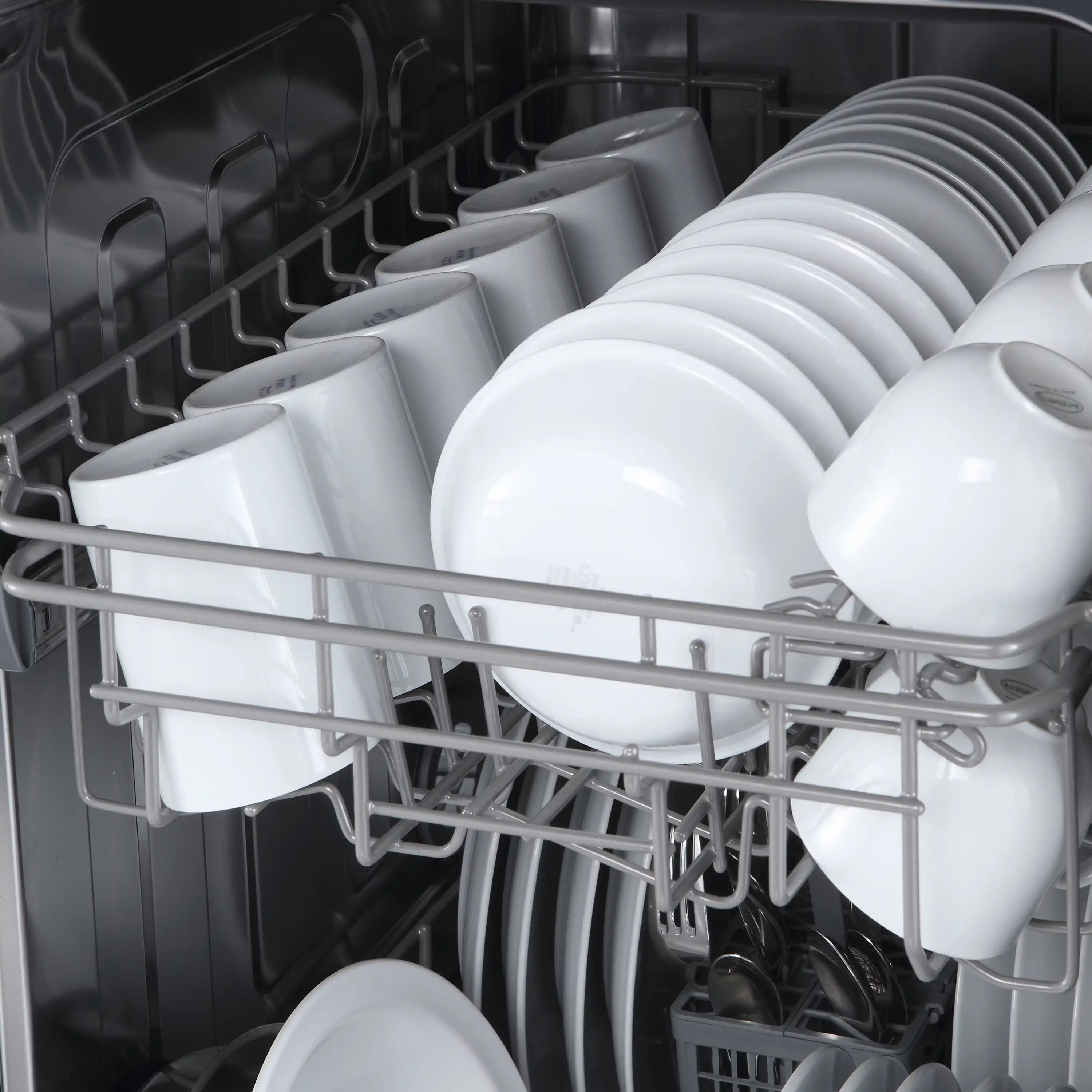 Dishwasher interior close-up with white plates, bowls, and cups on racks