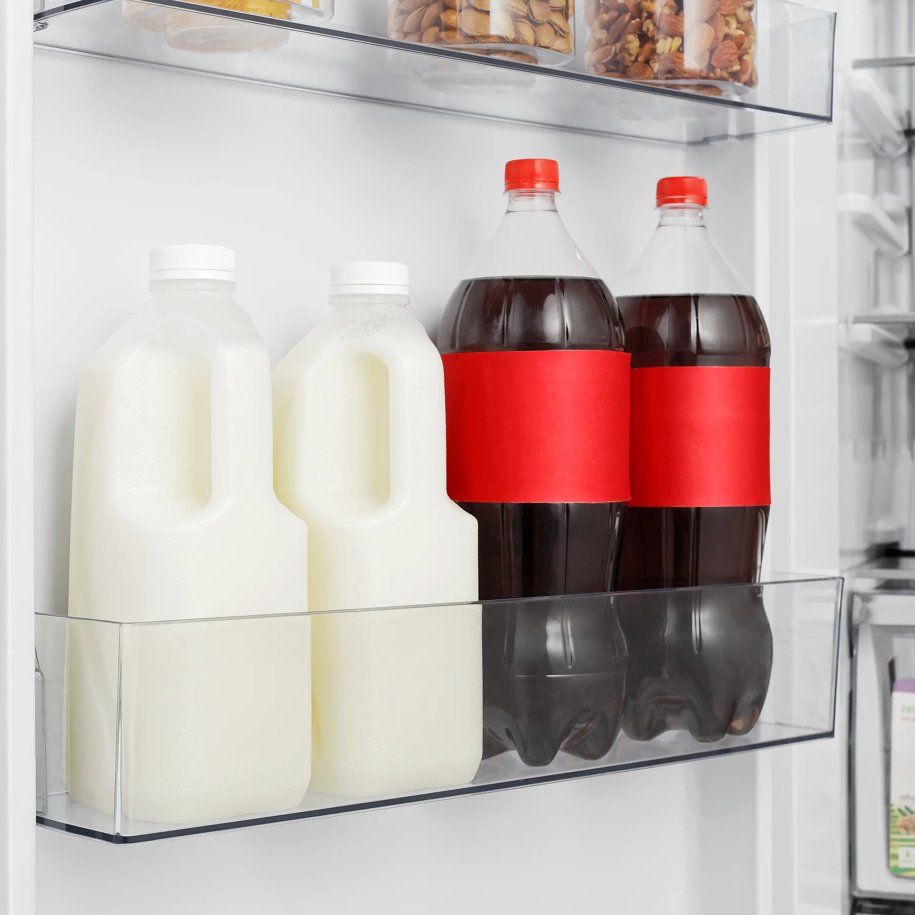 Refrigerator shelf with glass bottles of milk and dark drinks behind clear partition