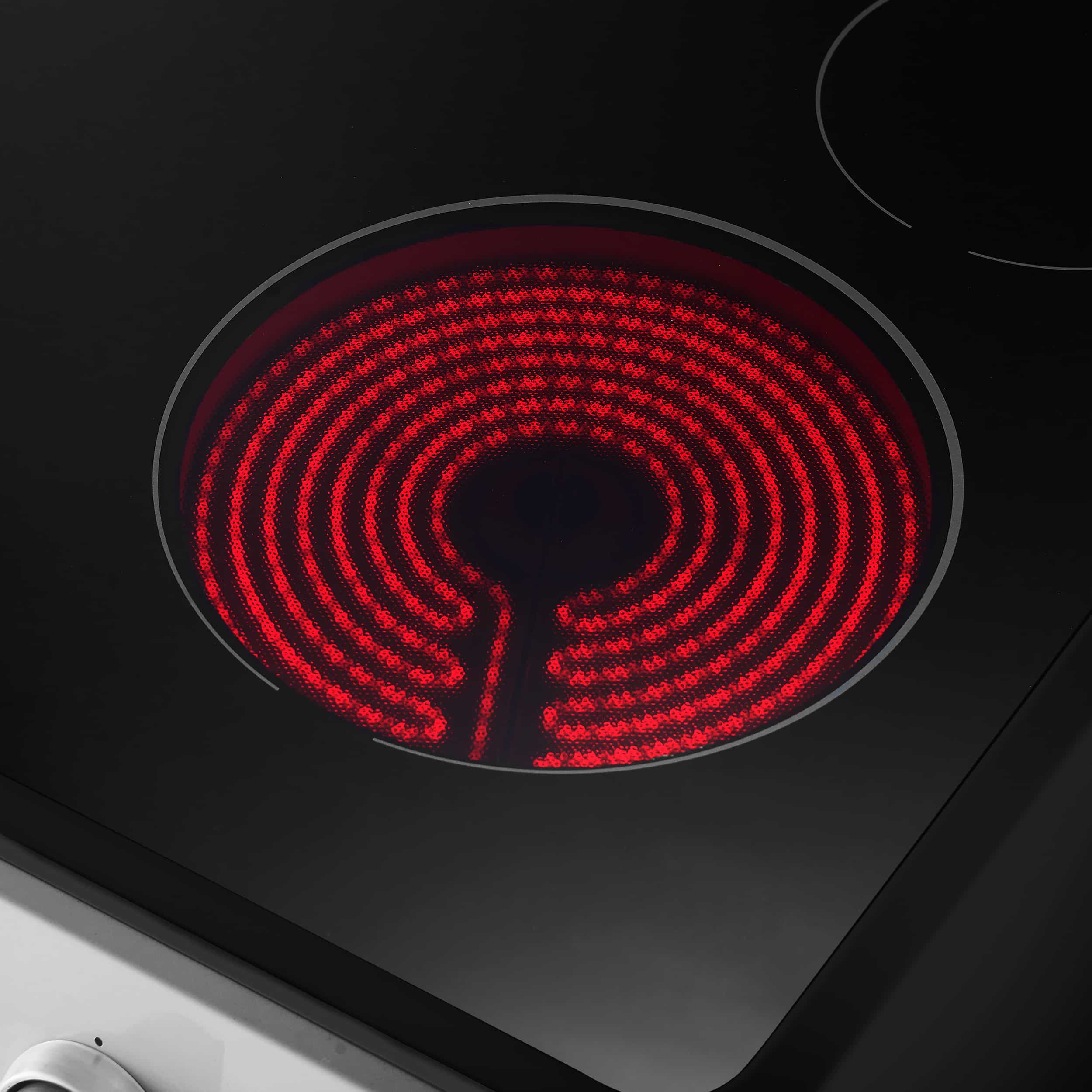 Electric cooktop burner glowing red on black glass surface