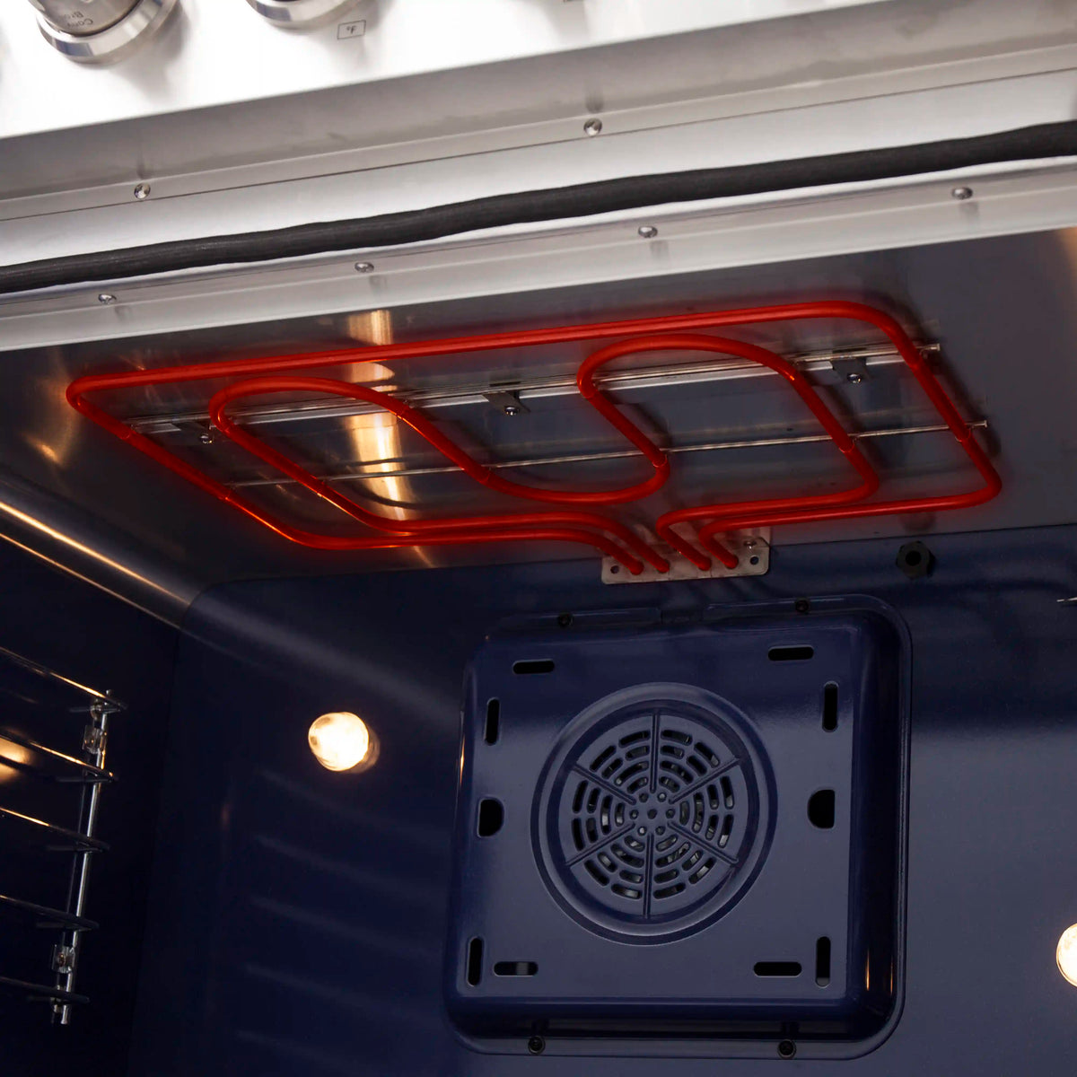 Inside electric oven with red glowing heating element and fan vent panel on back wall