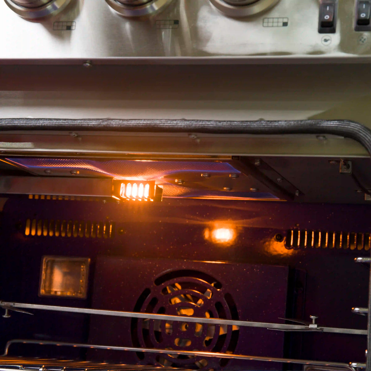 Close-up of lit burner inside dual-oven gas range with glowing heating element