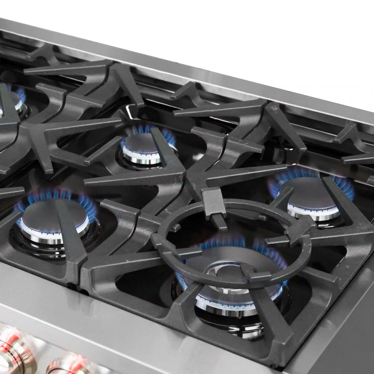 Close-up of stainless steel gas cooktop with black grates and four lit burner caps