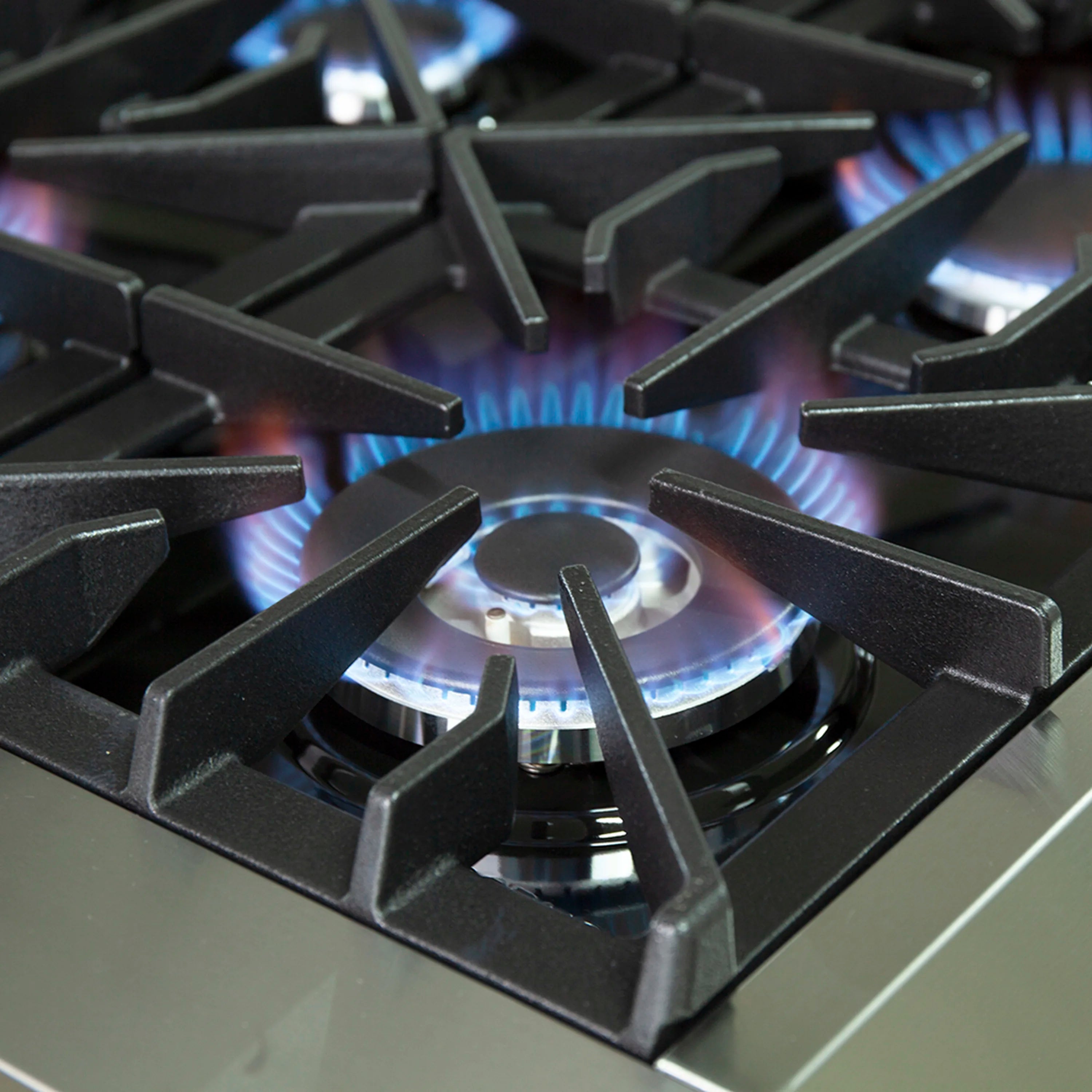Gas cooktop burner with blue flame under black grates